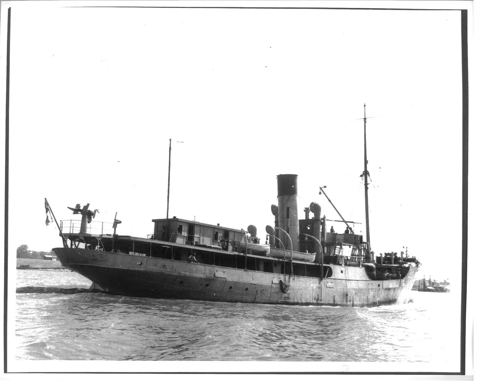 Historical black and white photo of a vintage military ship sailing on water, with a small island or land in the background.