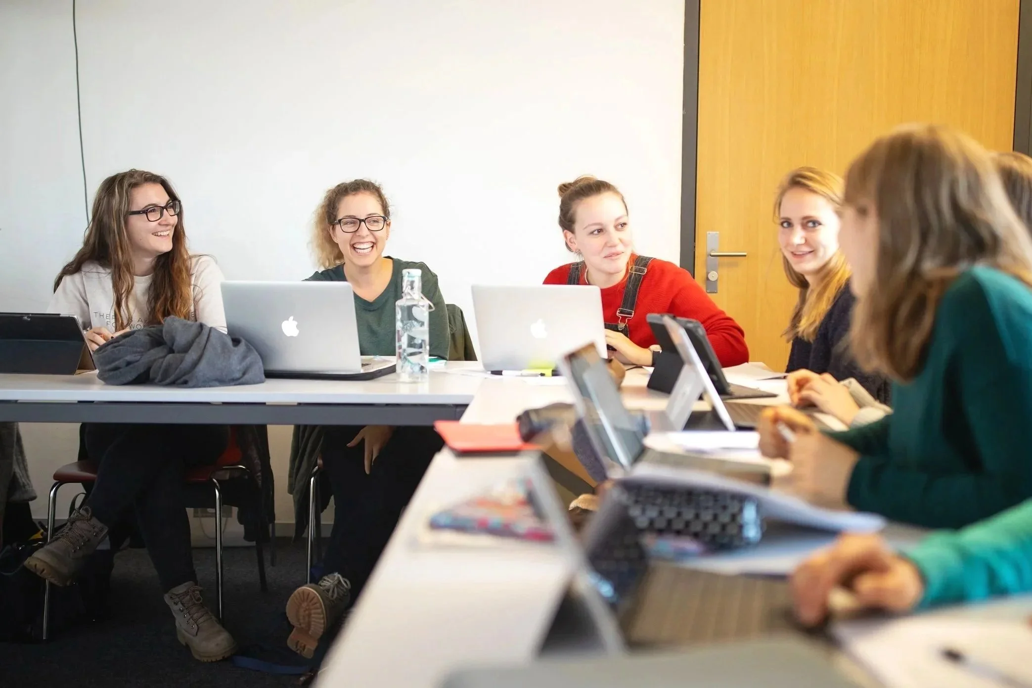 Groupe de femmes assises autour d'une table lors d'une réunion ou formation, utilisant des ordinateurs portables et discutant ensemble dans une salle de conférence.
