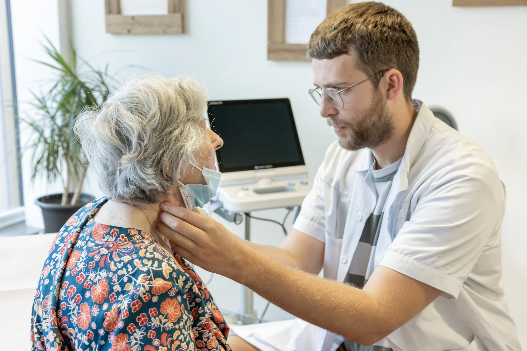 Un jeune homme en blouse blanche administre un vaccin ou une injection à une femme âgée portant un masque facial dans un cabinet médical.