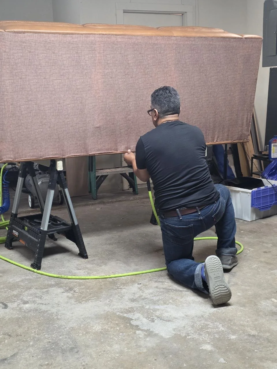 Professional upholsterer installing a dust cover on a custom sofa during the furniture reupholstery process in Dallas, Texas.