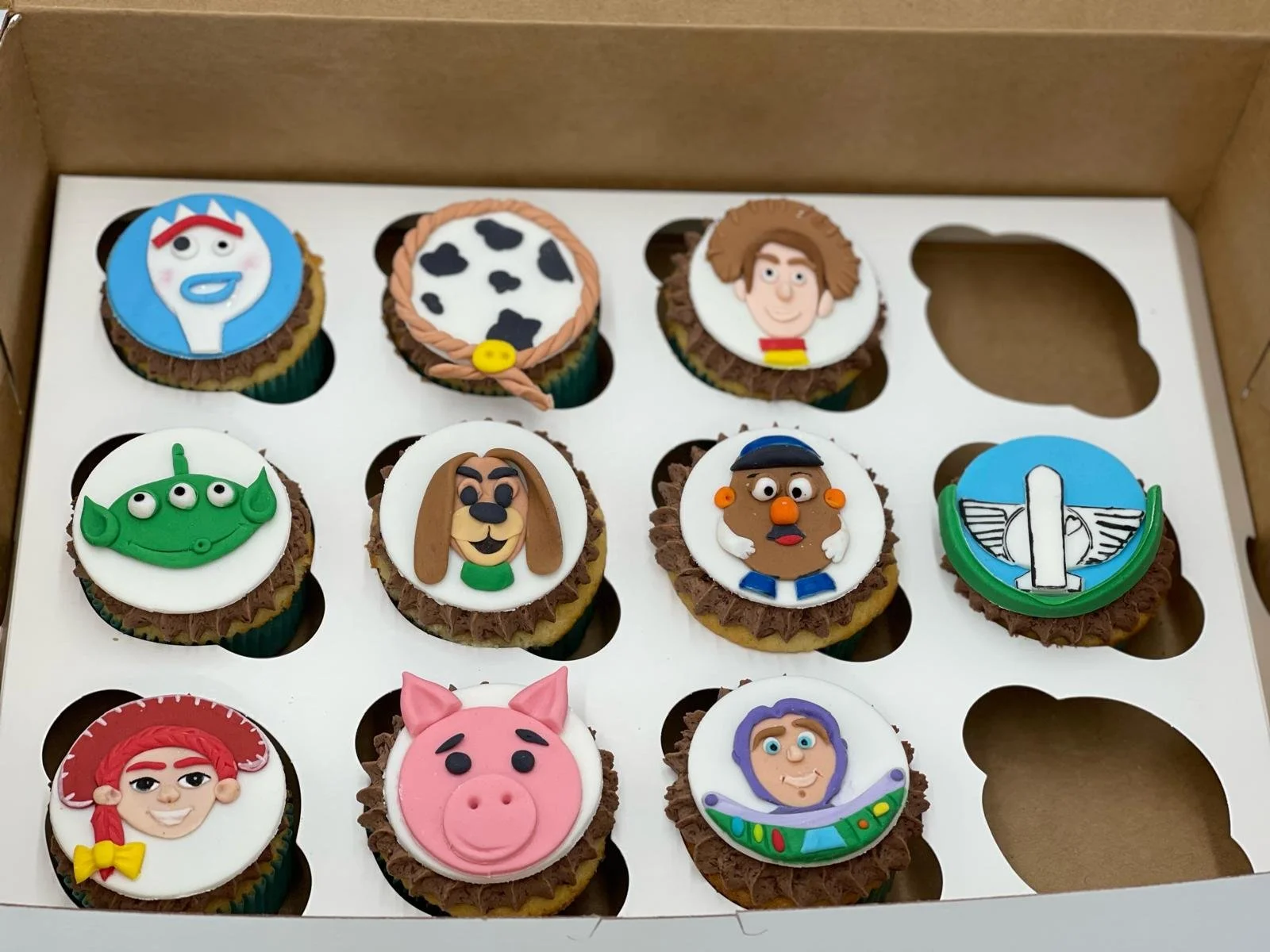 Collection of cupcakes decorated with characters from Toy Story, including Buzz Lightyear, Woody, Jessie, Mrs. Potato Head, Bo Peep, and Rex.
