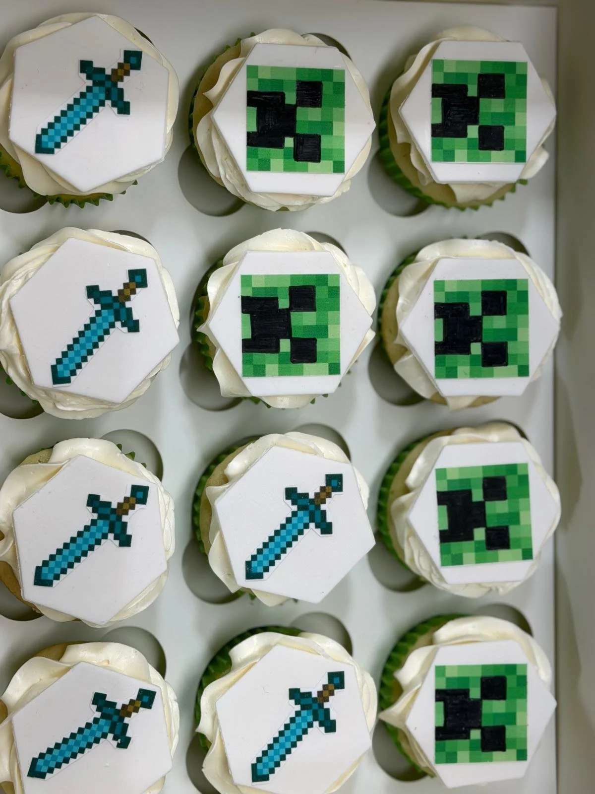 Cupcakes decorated with pixel art themed to Minecraft, featuring icons of a sword and a creeper face.
