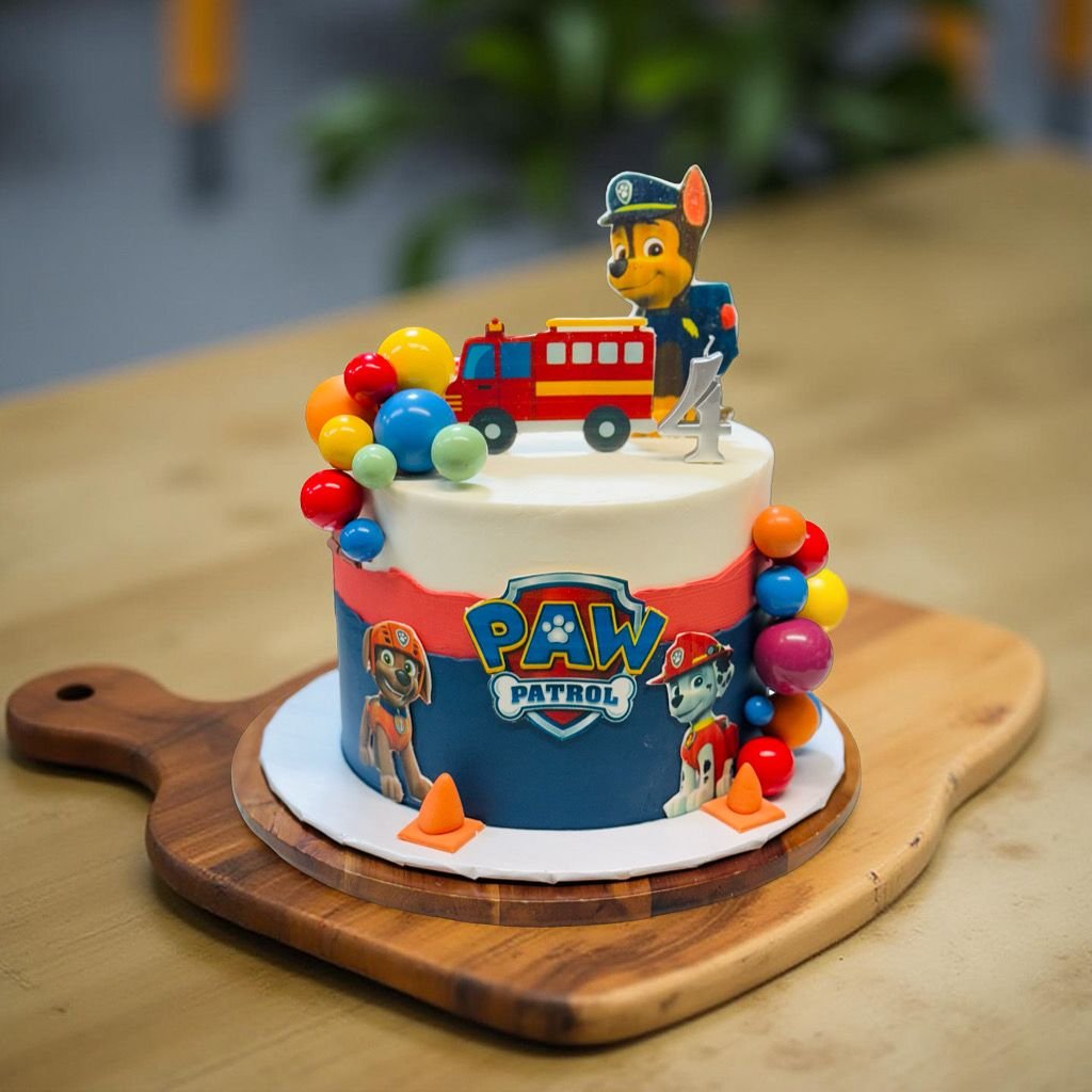 Paw Patrol-themed birthday cake with a firefighter paw patrol character on top, colorful decorations, and paw patrol images on the side, placed on a wooden board.