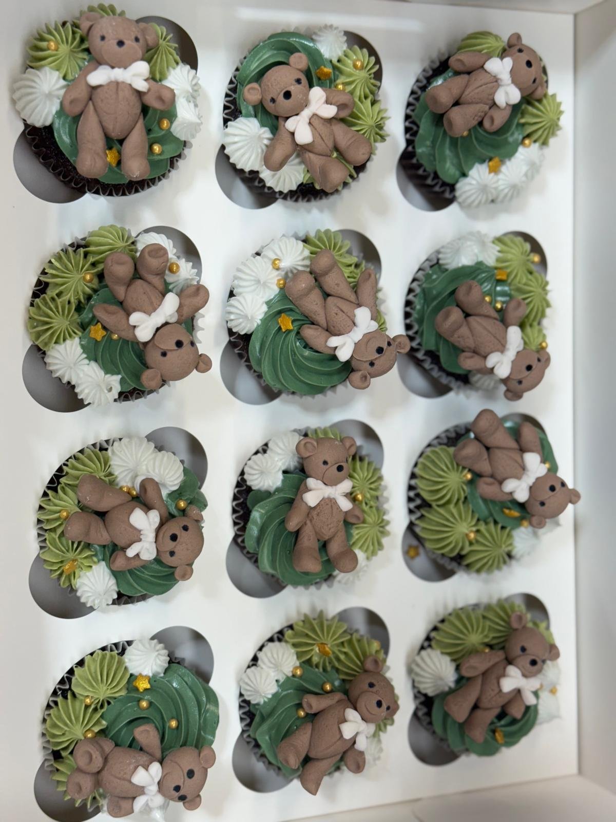 Box of cupcakes decorated with teddy bear toppers and green, white, and yellow frosting swirls.
