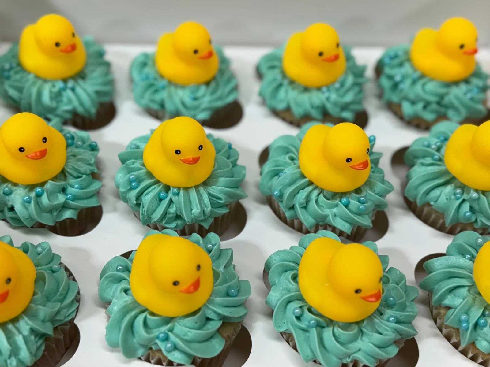 Easter-themed cupcakes decorated with green frosting, small blue sugar beads, and yellow rubber duck toppers.