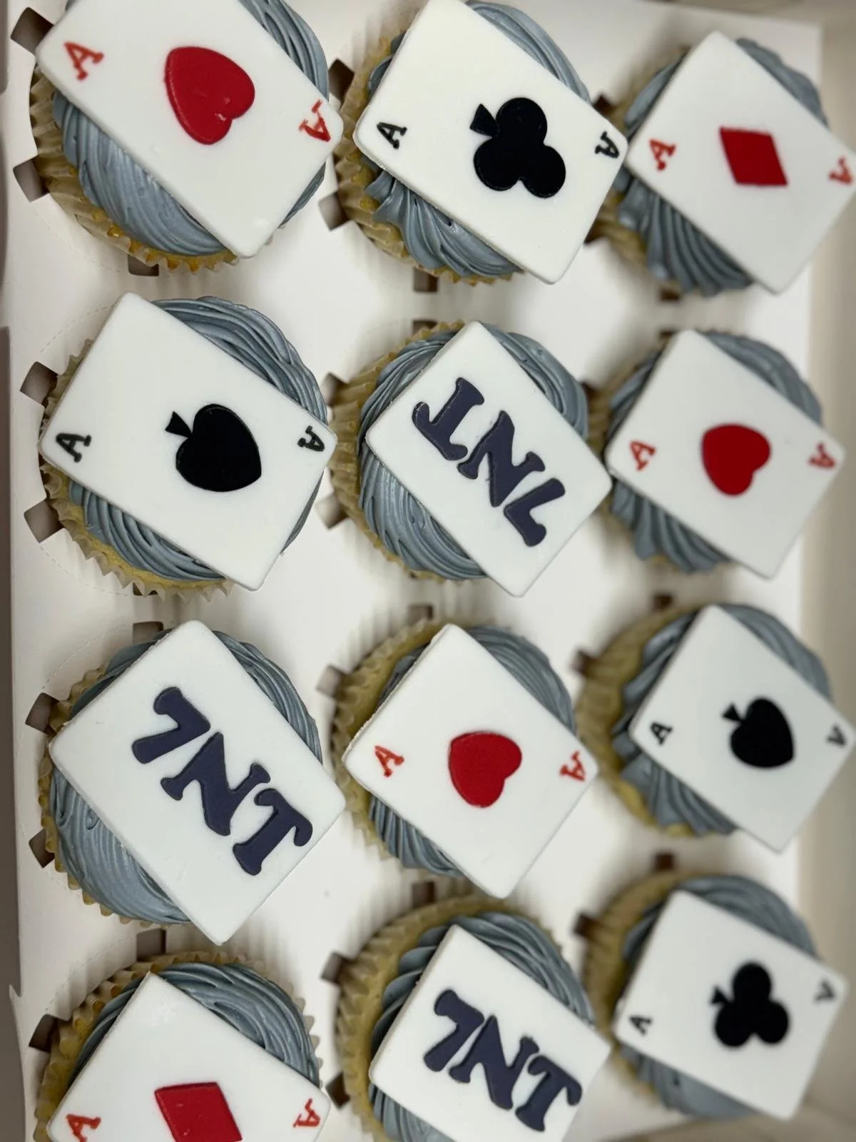 Cupcakes decorated with playing card themes, including aces and the word 'JAIL' on fondant toppers, with gray piping around the edges.