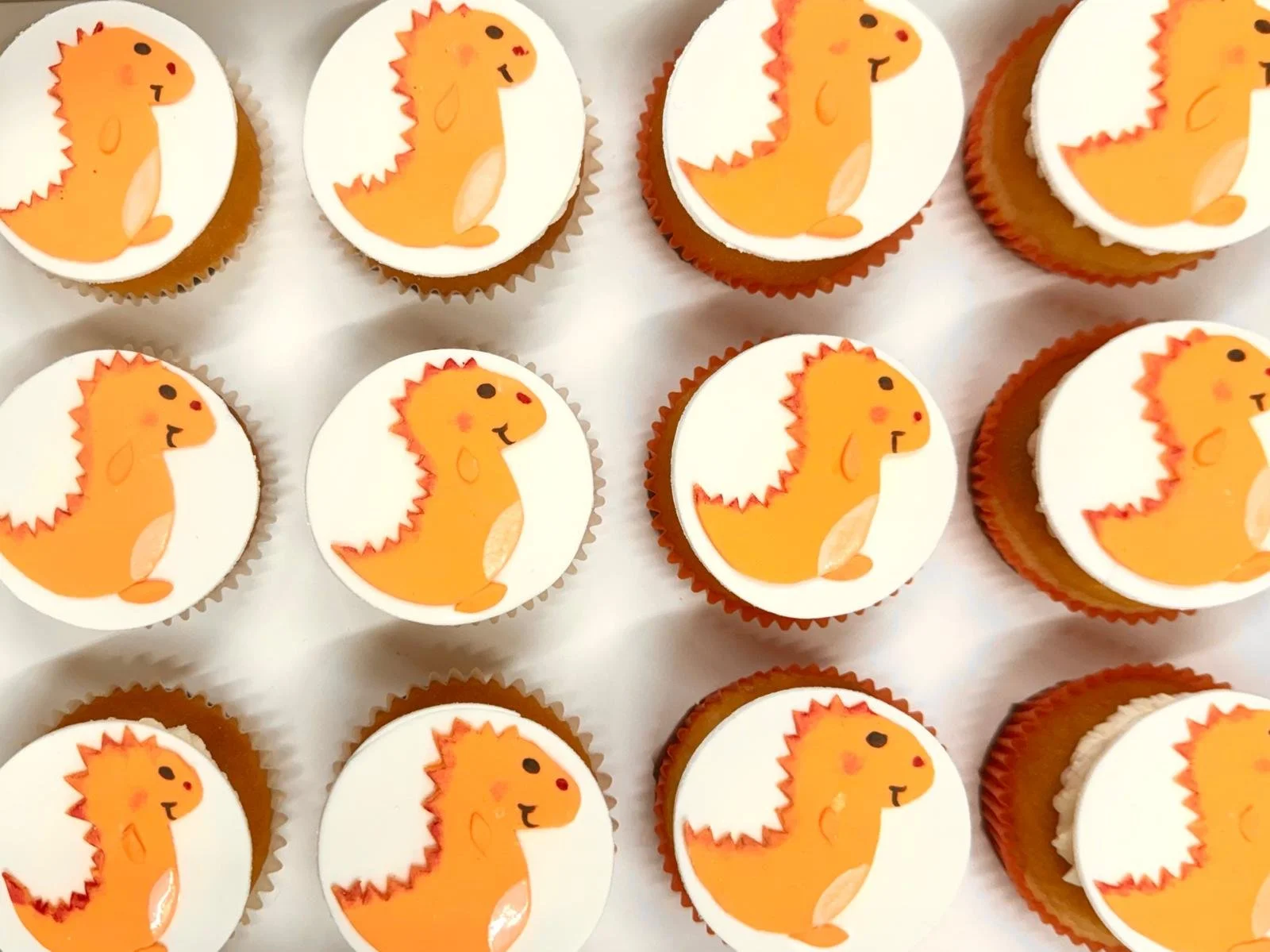 Cupcakes with toppers featuring a cartoon orange dinosaur on a white background.
