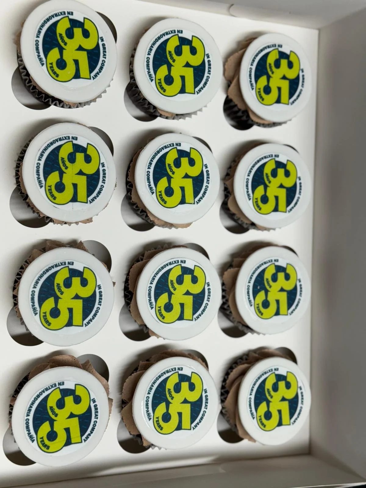 Group of cupcakes with printed toppers featuring the number 35 in yellow and blue text, arranged in a grid on a white surface.