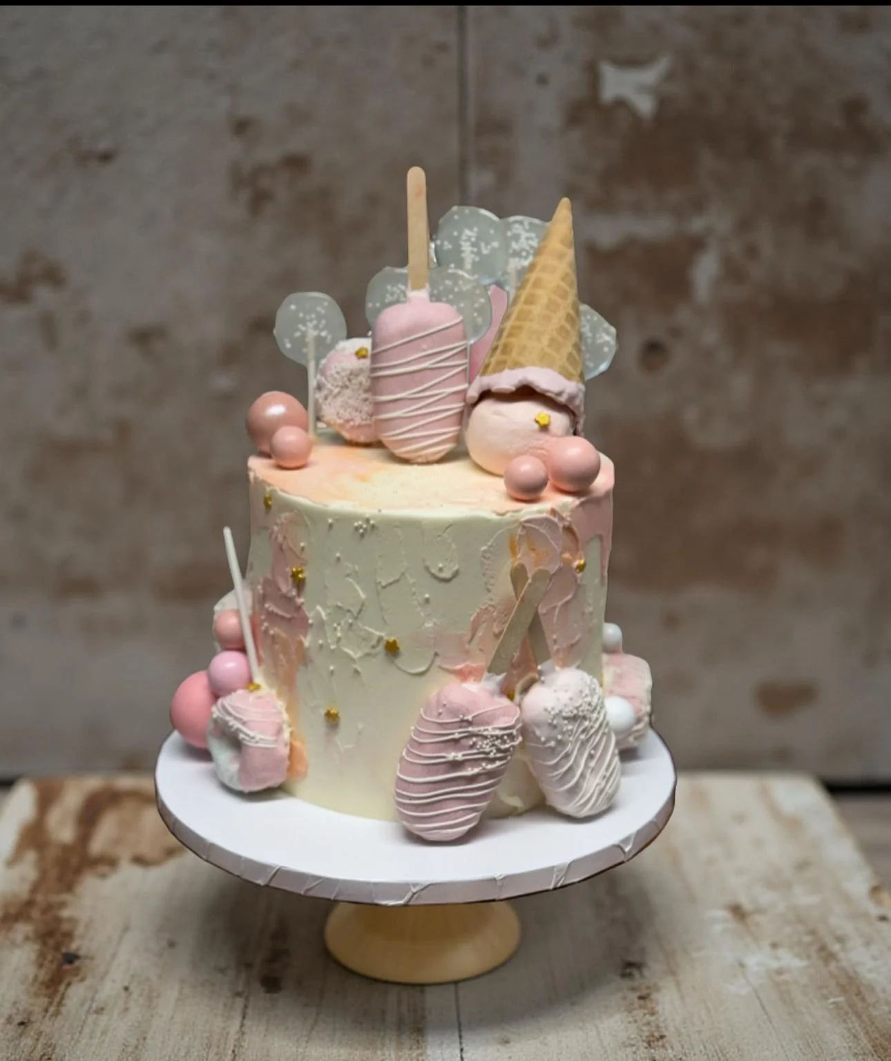 A pastel-colored cake decorated with ice cream cone, ice cream bars, and pink and white spheres on top and around the sides.