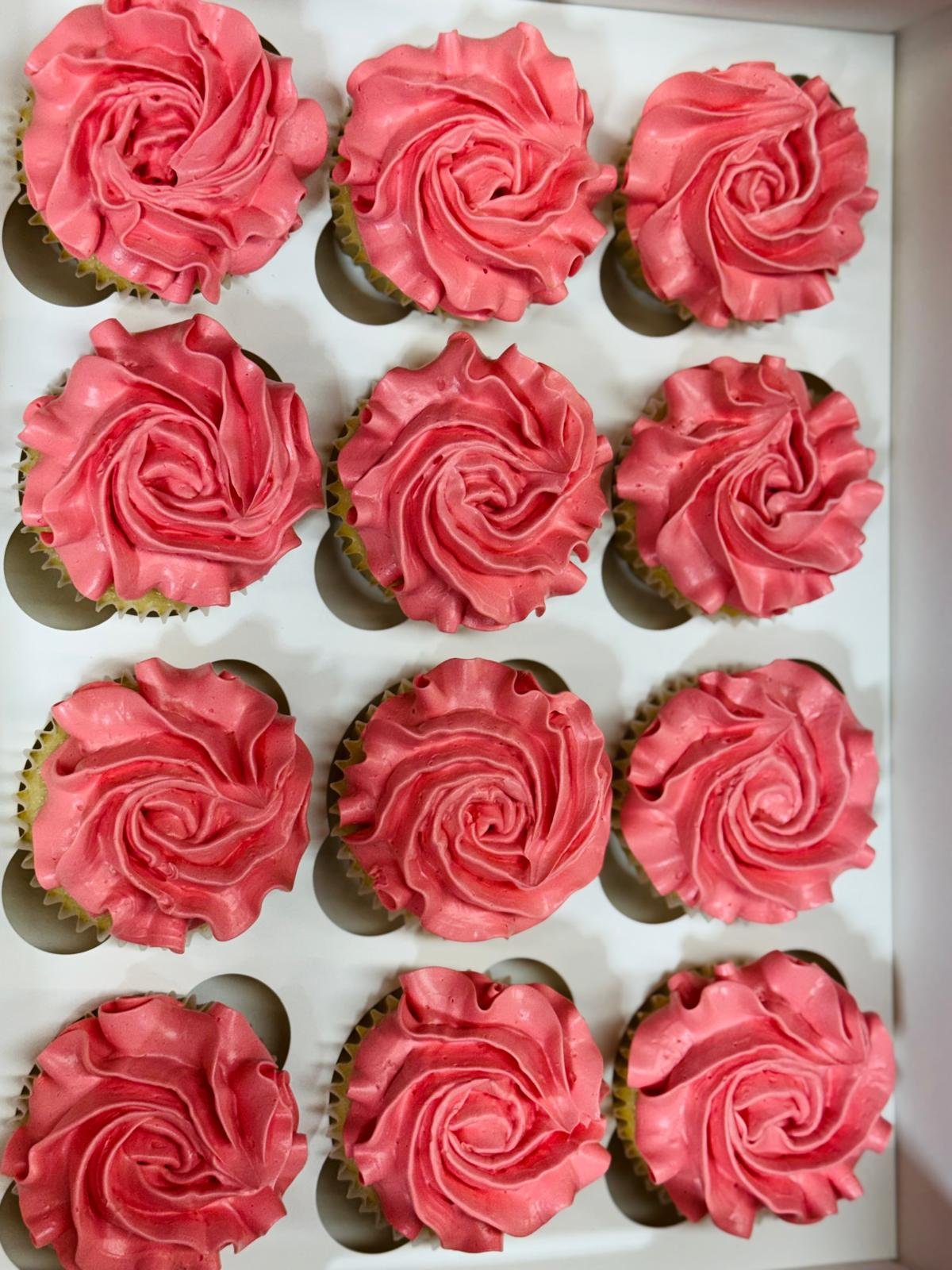A tray of twelve cupcakes with pink, swirled frosting designed to look like roses.
