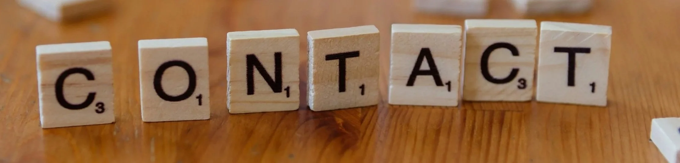 Scrabble tiles spelling out the word 'CONTACT' on a wooden surface.
