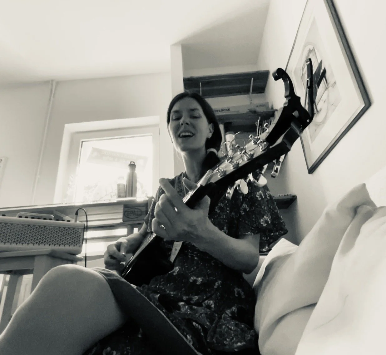 Frau spielt Irish Bouzouki in einem Wohnzimmer, sitzend auf einem Sofa, schwarz-weiß Foto.