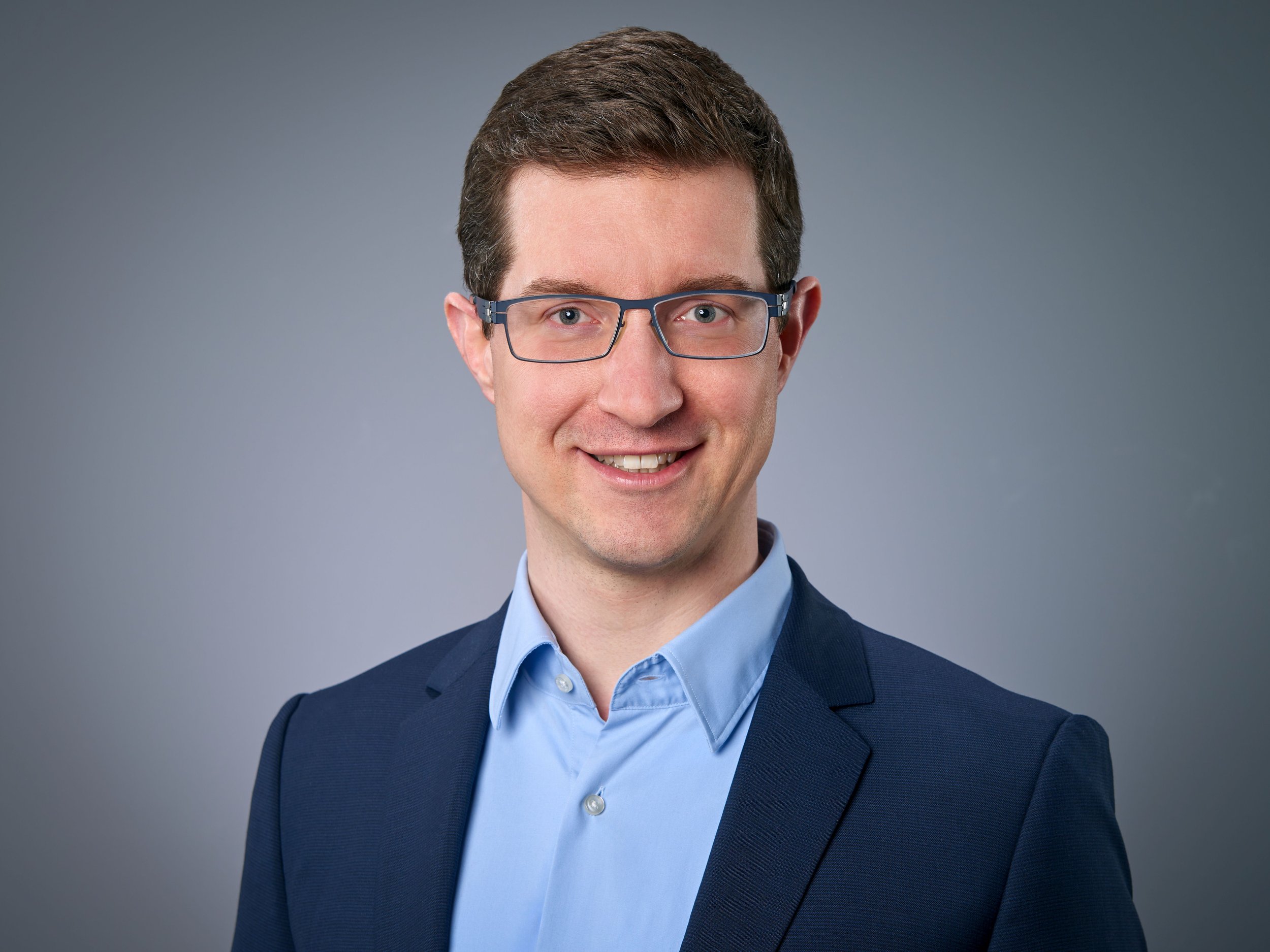 Felix Knittel, Gründer von FührGesundheit, lächelnd im Halbporträt vor grauem Hintergrund