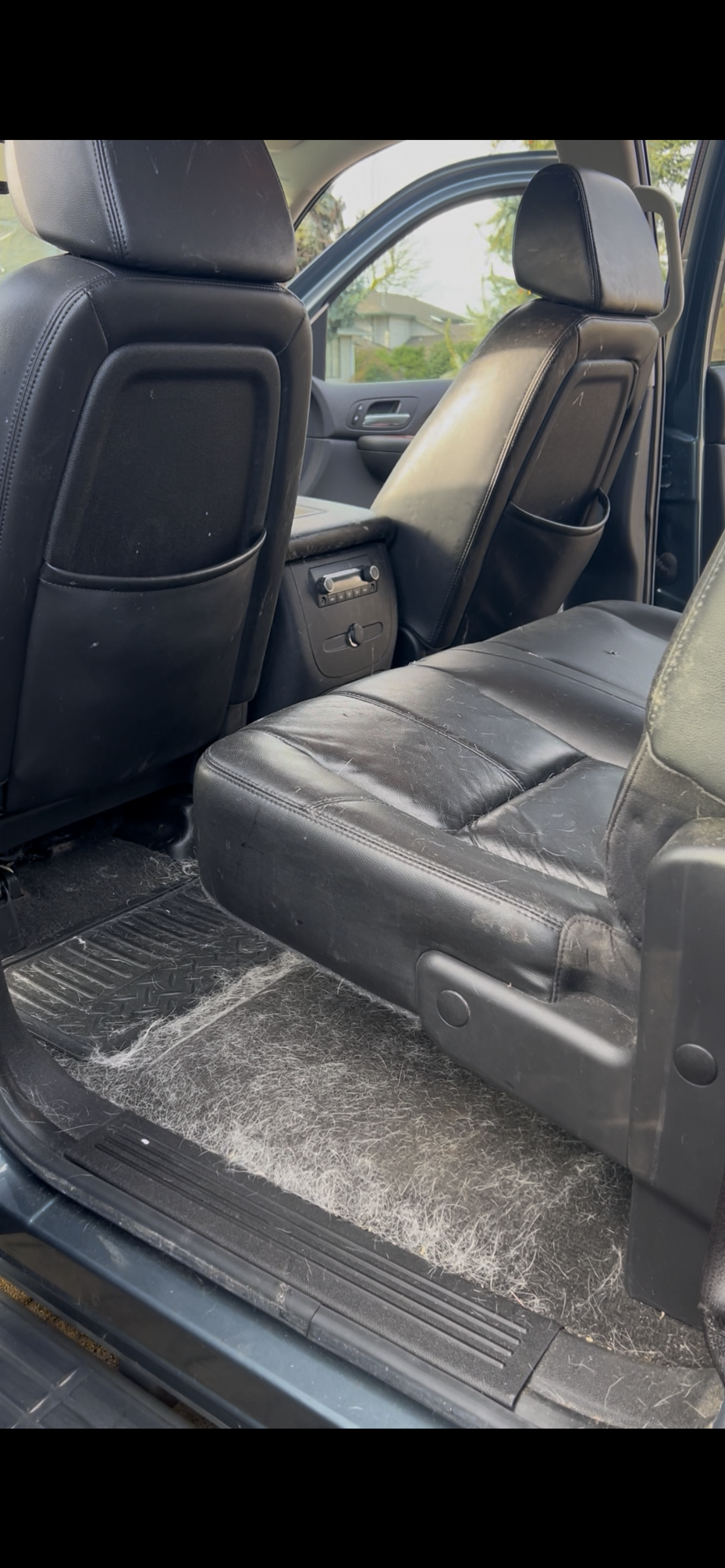 The interior of a vehicle showing the back seat with black leather upholstery that is worn and scuffed, and a dirty floor mat.