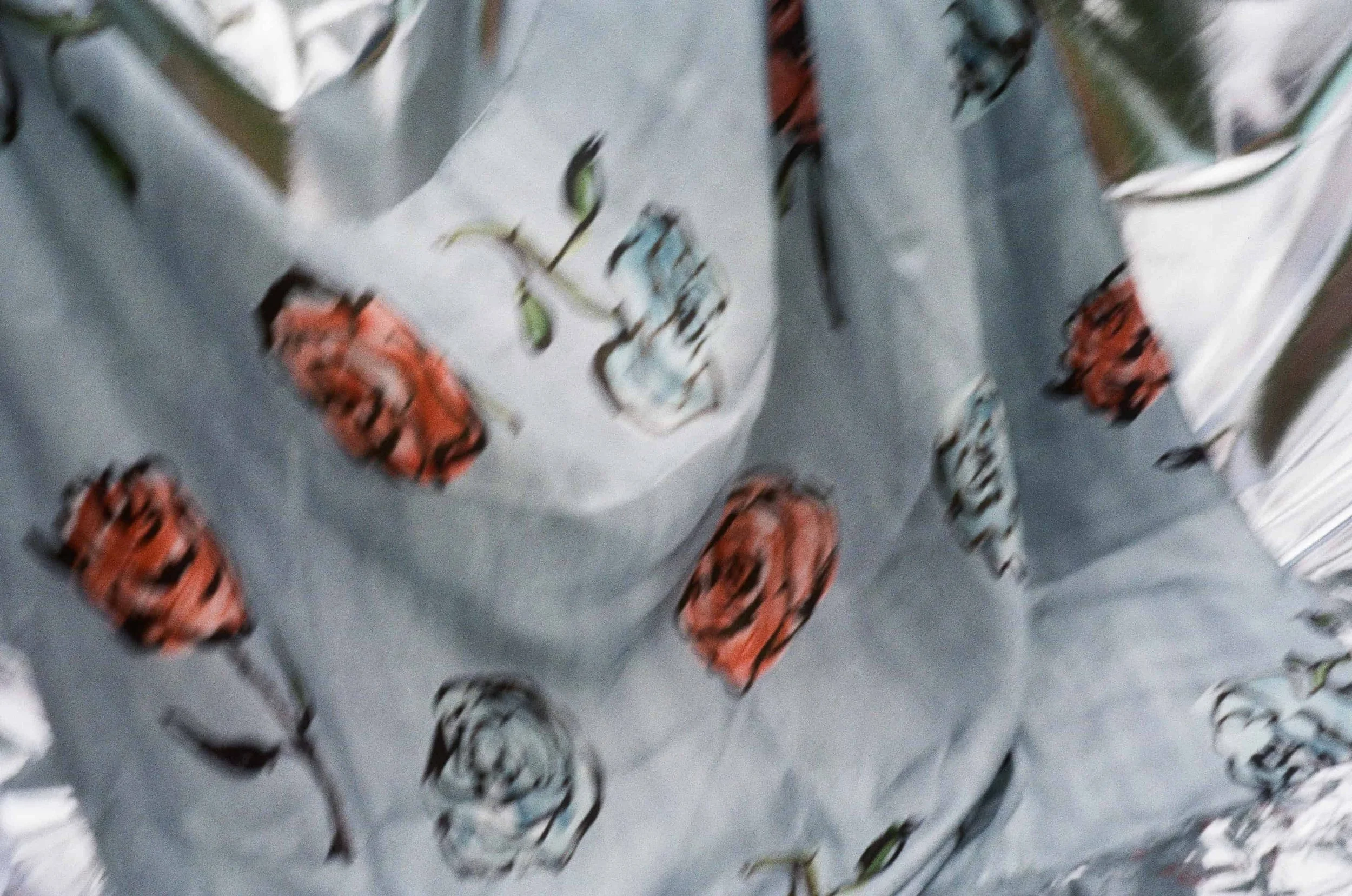 Blurred close-up of a patterned fabric with black, orange, and green designs on a white background.