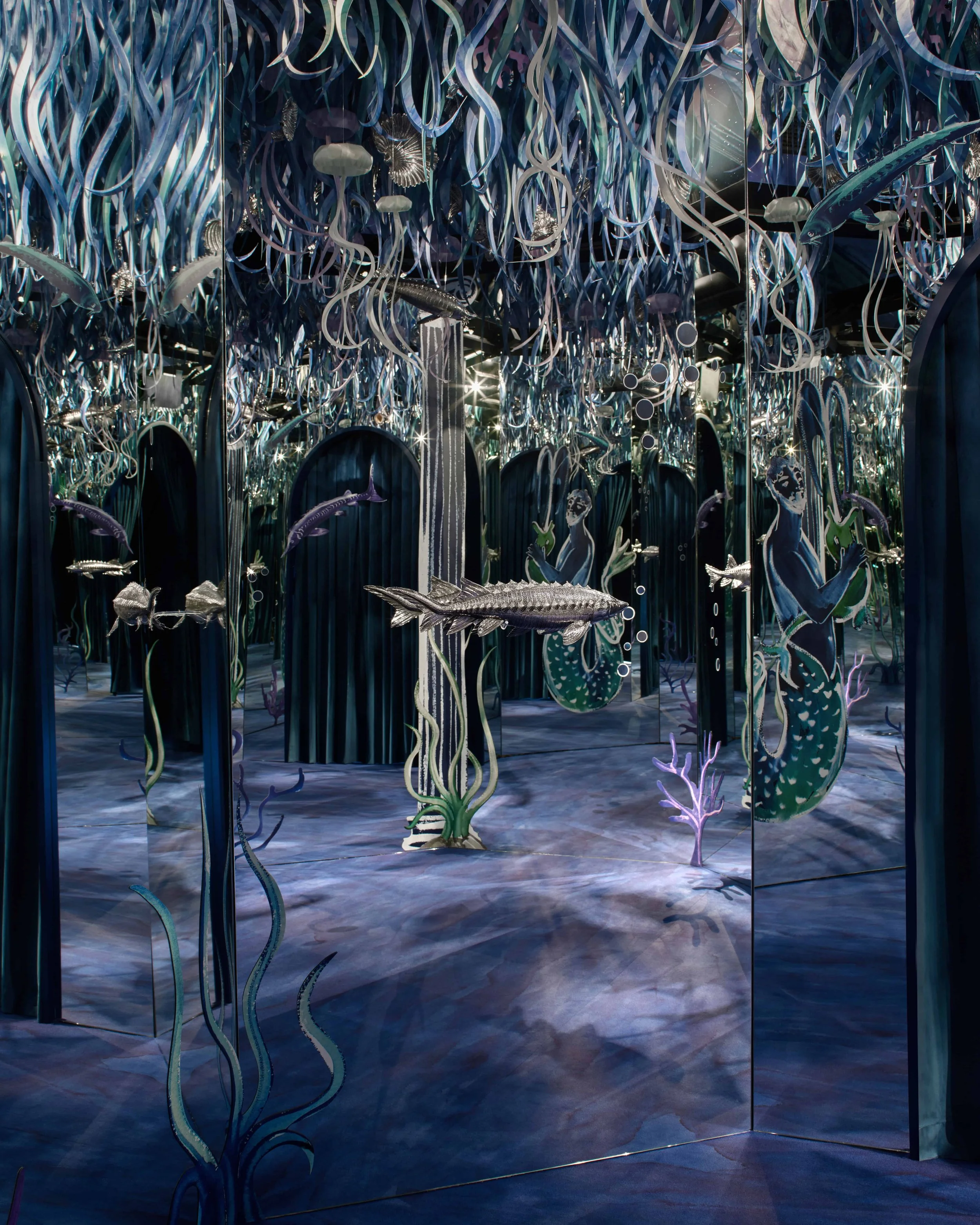 An underwater-themed art installation featuring holographic seaweed, jellyfish, and fish reflections in mirrors, creating an immersive ocean scene.