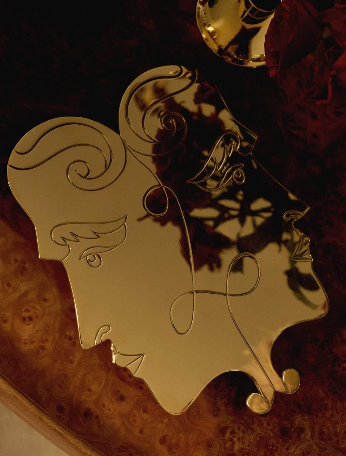 Decorative mirror with a silhouette of a woman's face, placed on a wooden surface with a dark red cloth nearby.