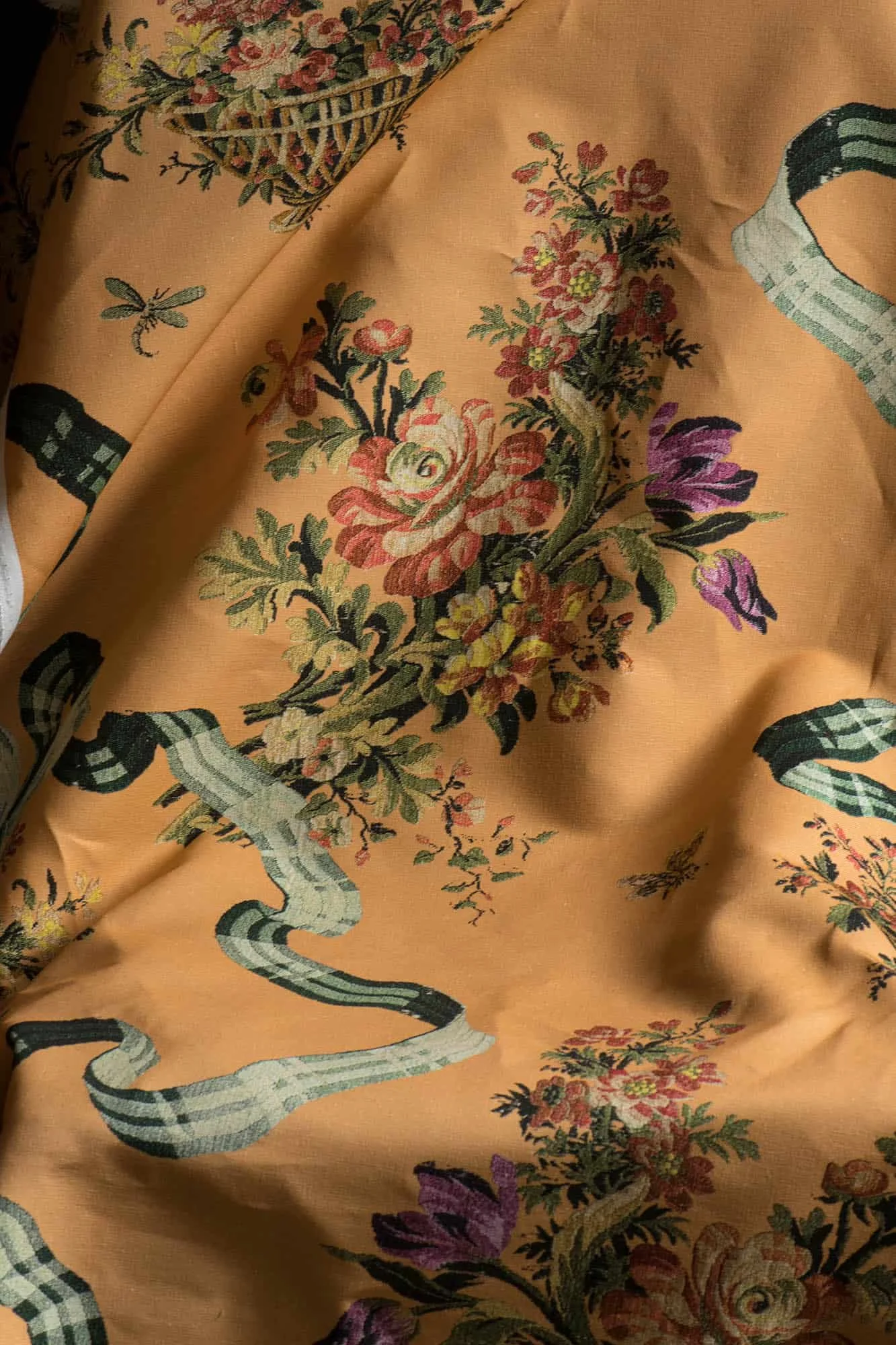Close-up of an ornate fabric with a floral and dragon pattern in muted colors on a peach-colored background.