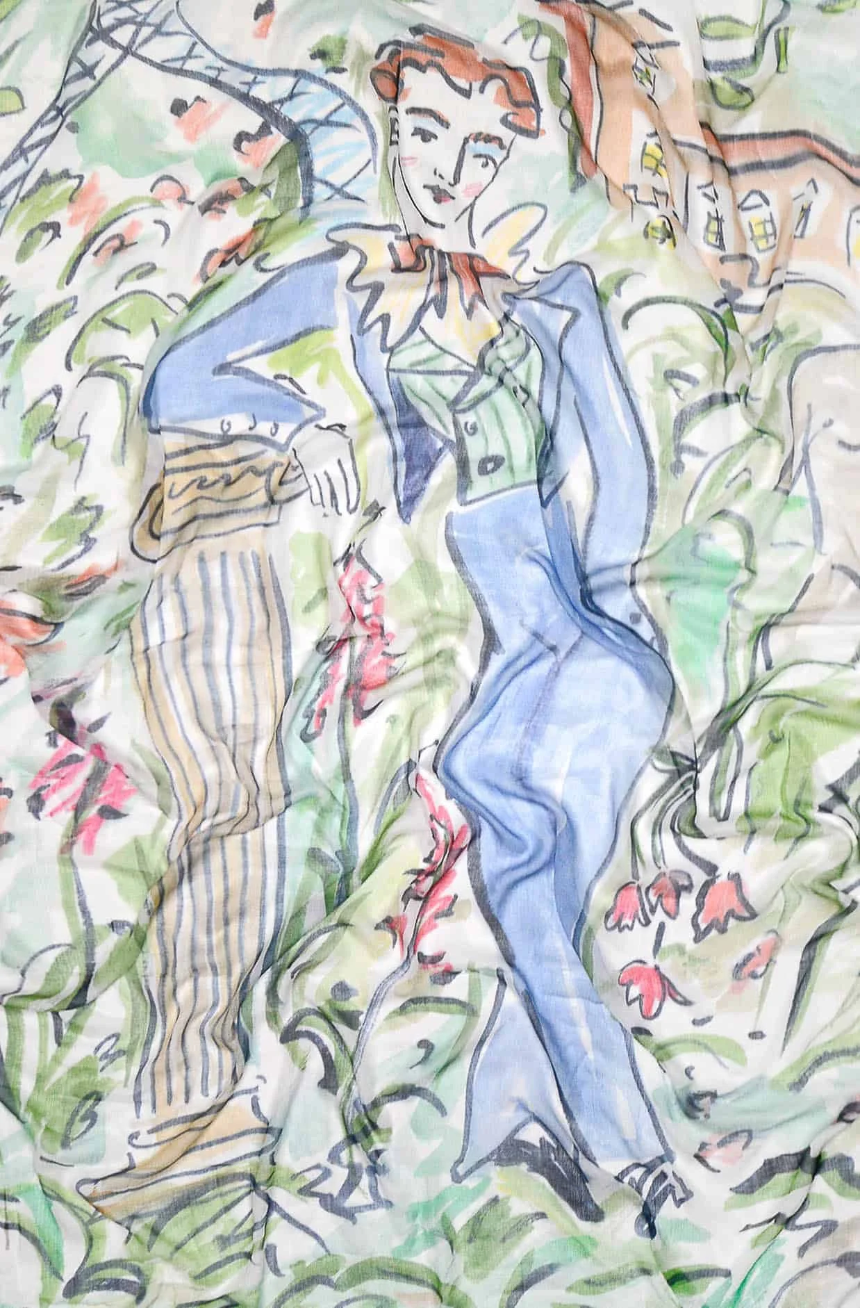 A colorful illustration on fabric featuring a woman with red hair, wearing a blue jacket and green shirt, amid greenery and flowers.
