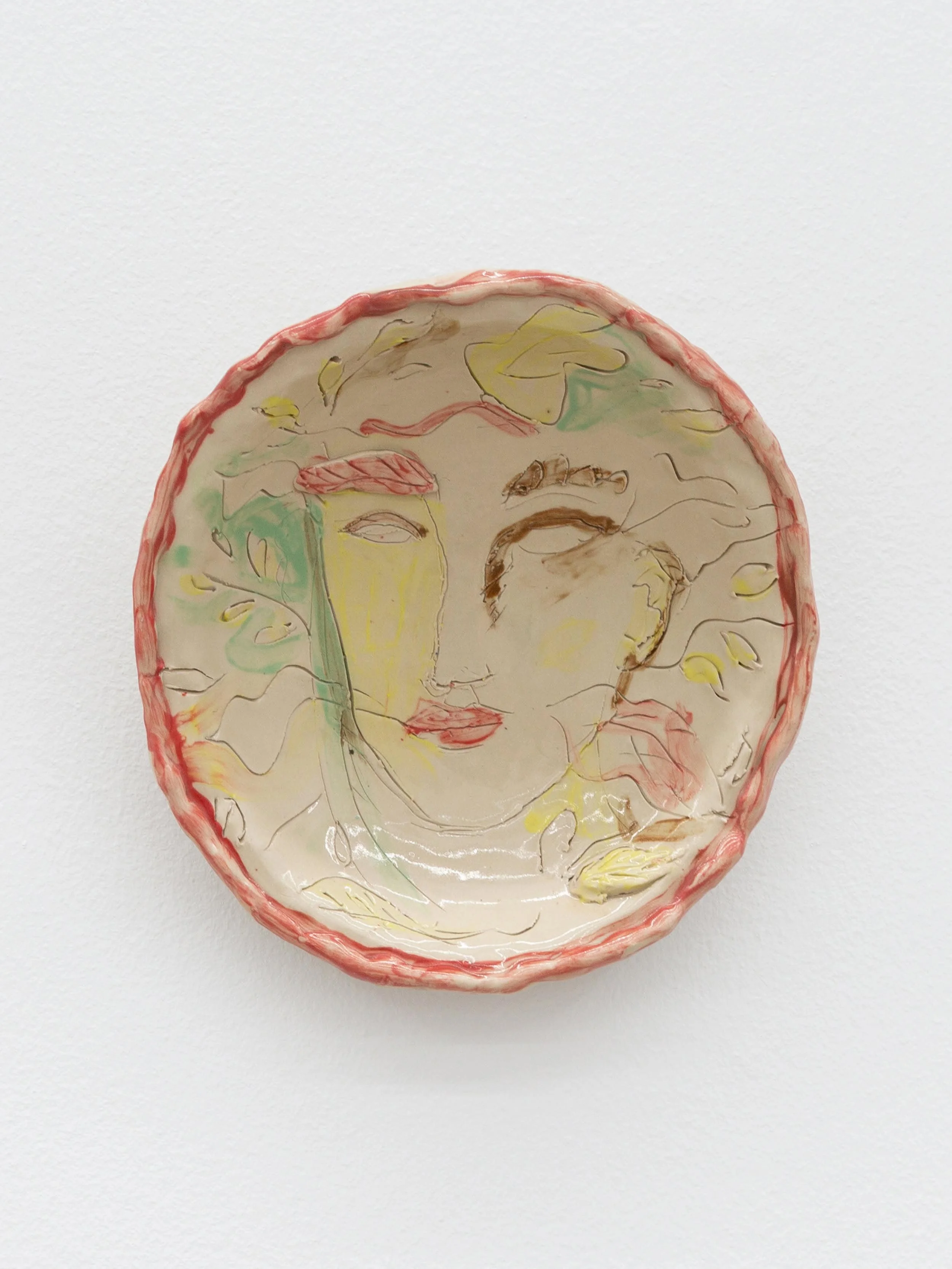A ceramic plate with a hand-painted abstract portrait of a woman's face, with a pink border and light colors including green, yellow, and brown.