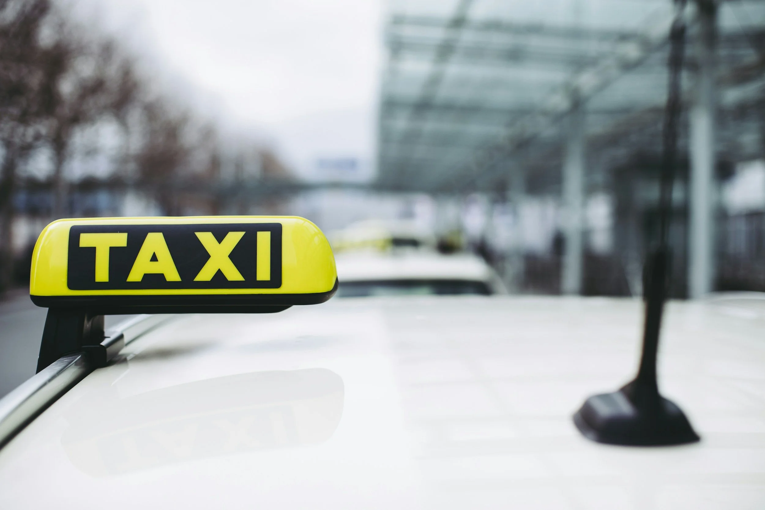 The front of a taxi cab with a yellow taxi sign on the roof, seen from inside the vehicle on a city street.