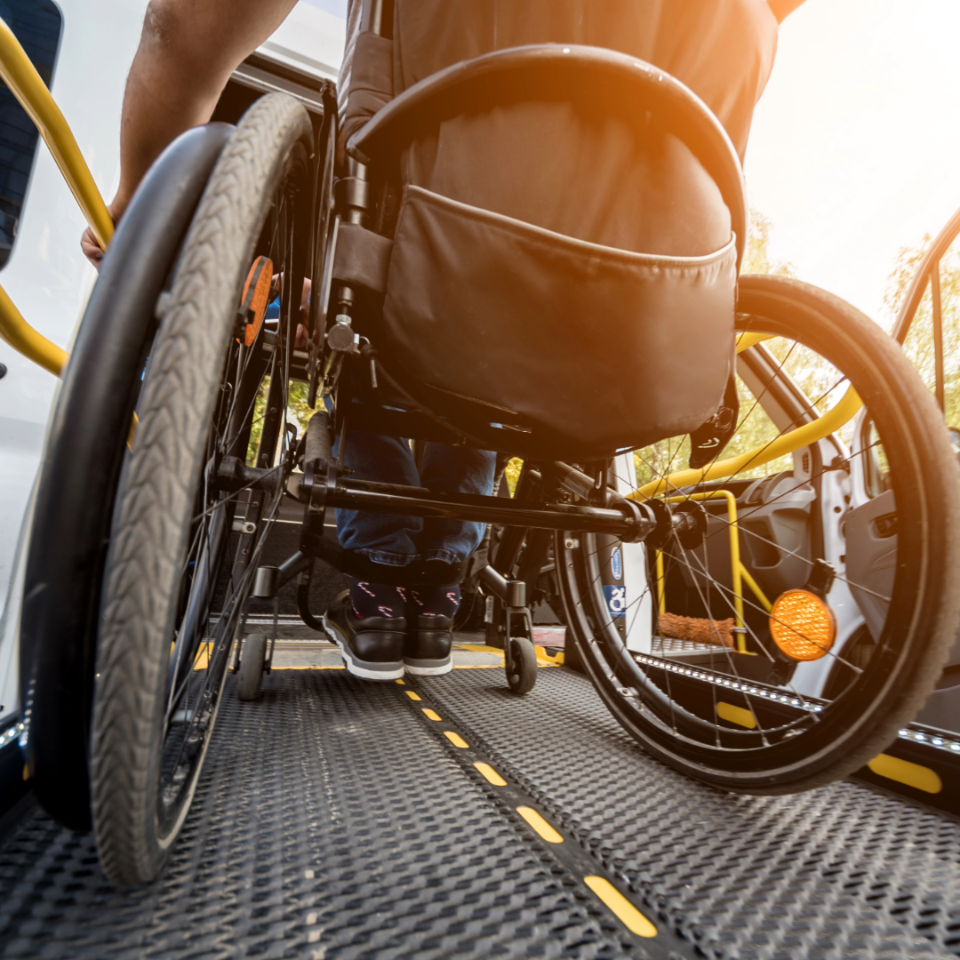 Close-up of a wheelchair on a vehicle ramp, with a person’s legs and shoes visible.