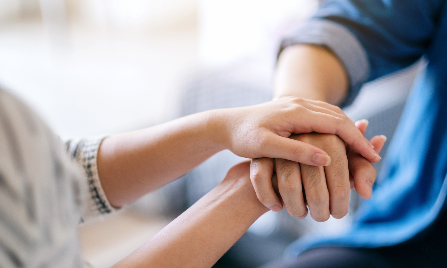 Two people holding hands in a supportive manner, with one person's hand resting on top of the other's.