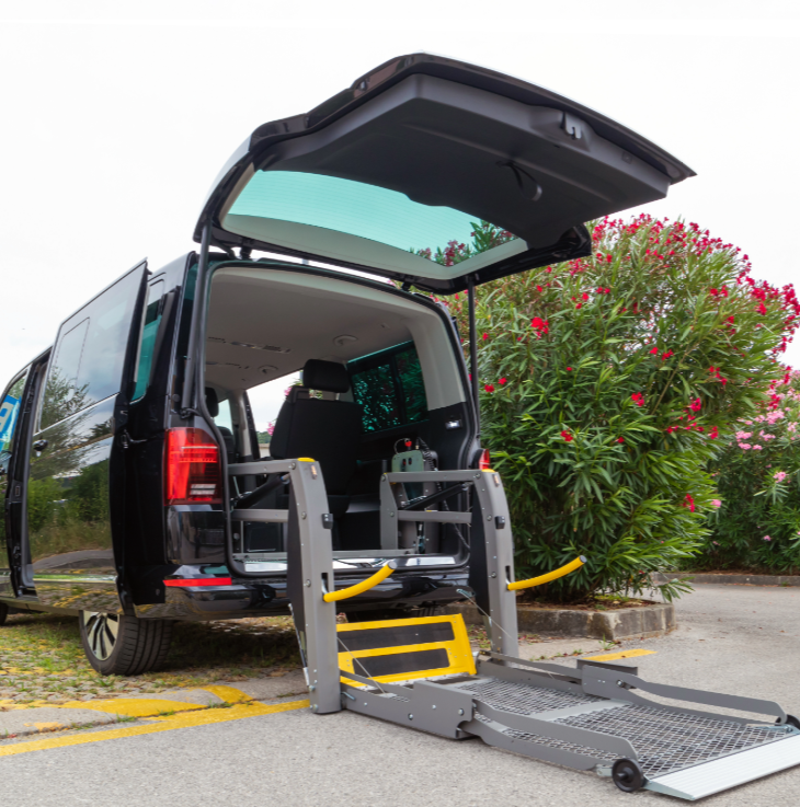 Black van with open rear door and wheelchair lift, parked near flowering bush.