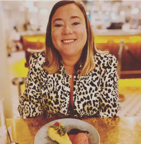 A woman with shoulder-length hair smiling at a restaurant table with a dessert plate in front of her.