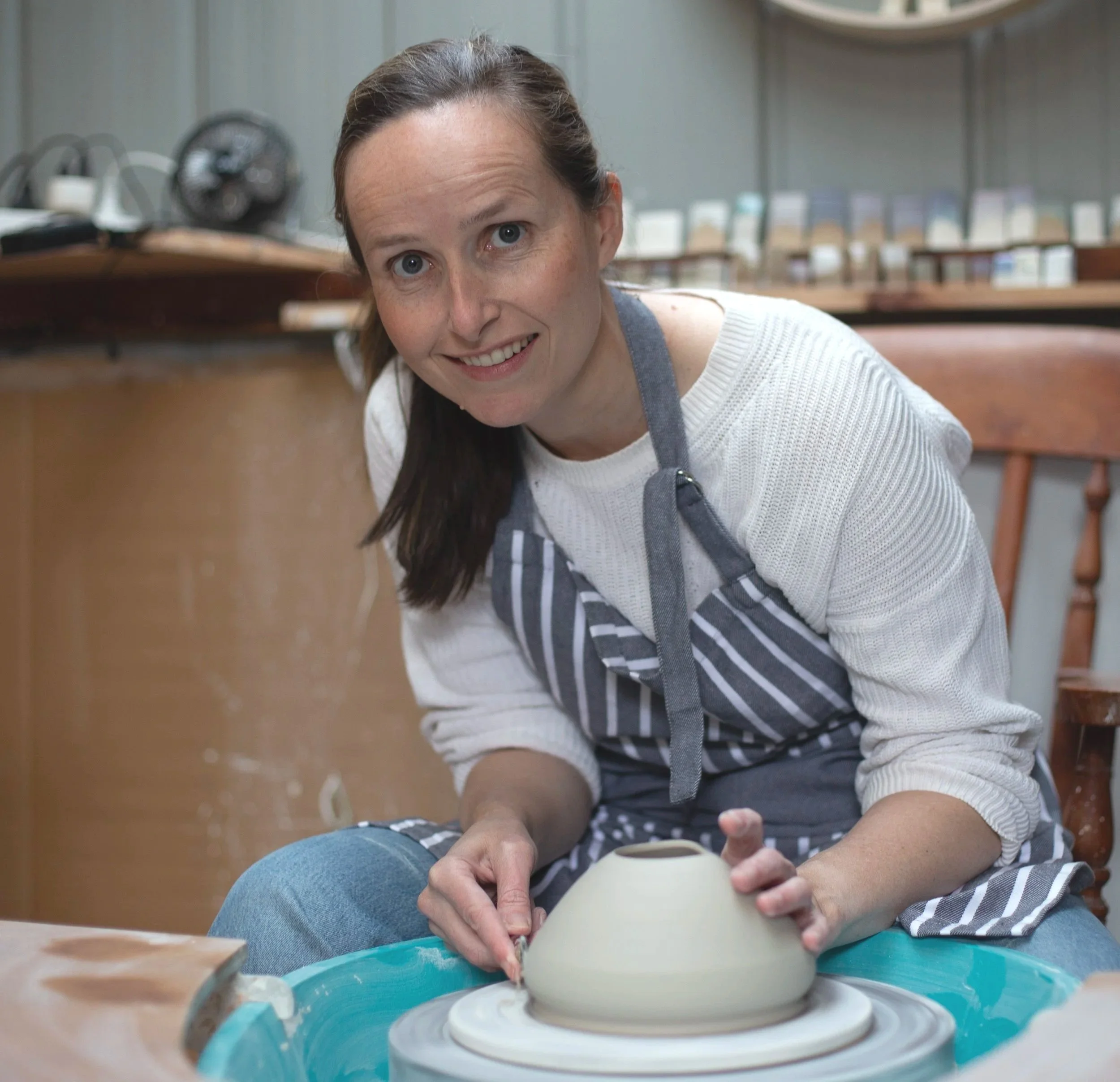 Woman at a pottery wheel shaping clay in a ceramic studio.