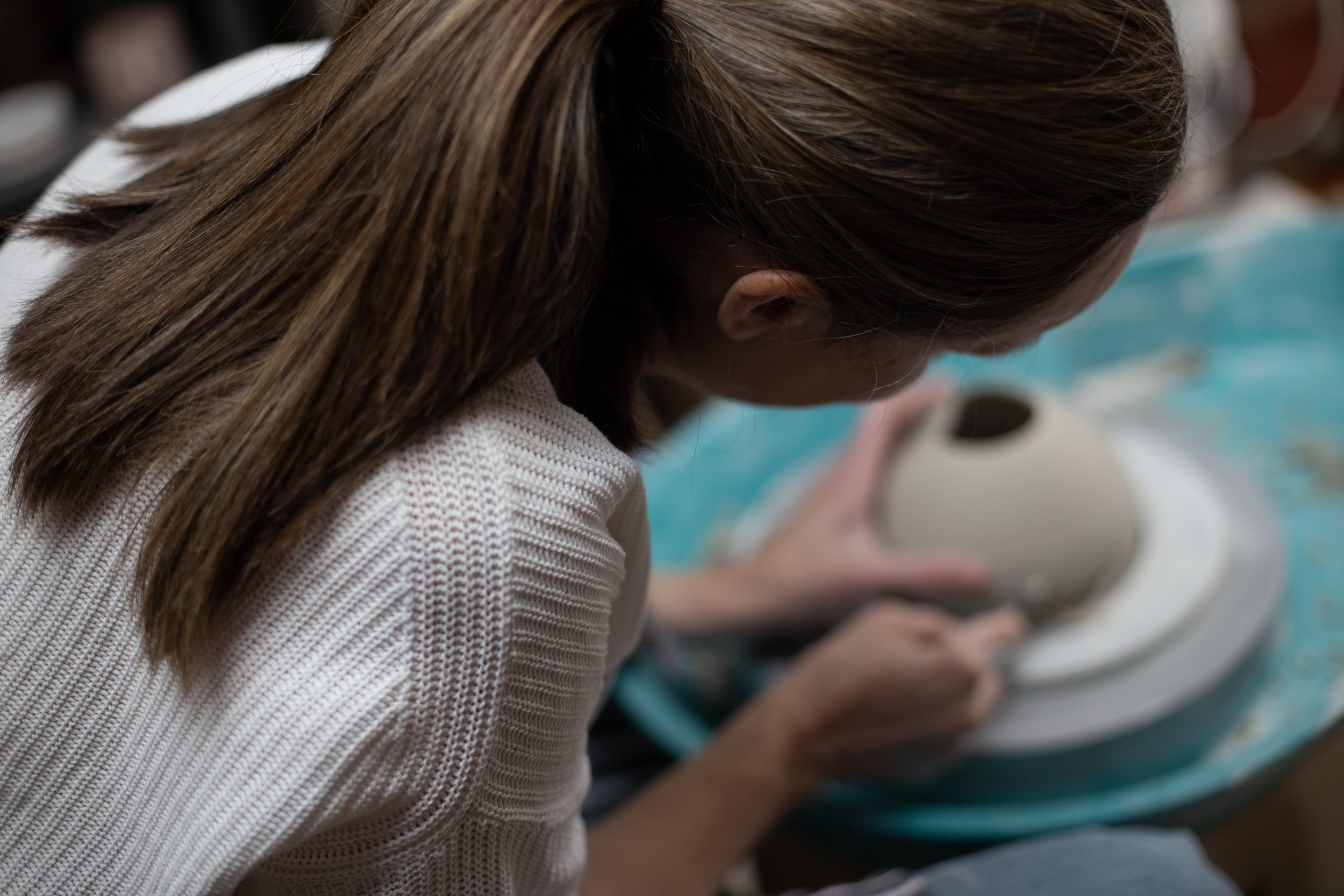 Close-up of a woman with long brown hair, wearing a white textured sweater, looking down while interacting with her smartphone.
