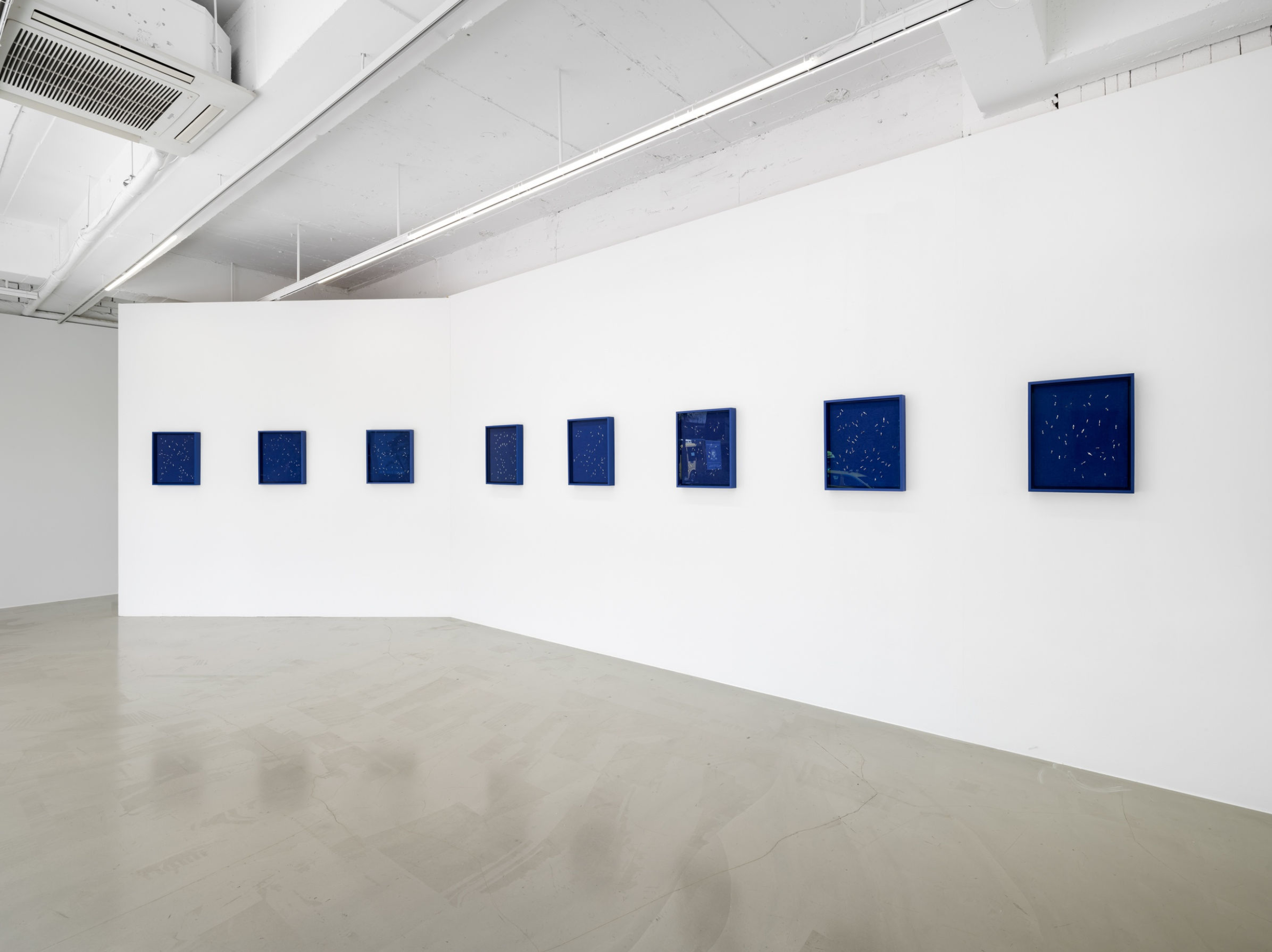 Gallery installation view of Burnsoo Song exhibition — small blue abstract works in horizontal sequence, white gallery walls
