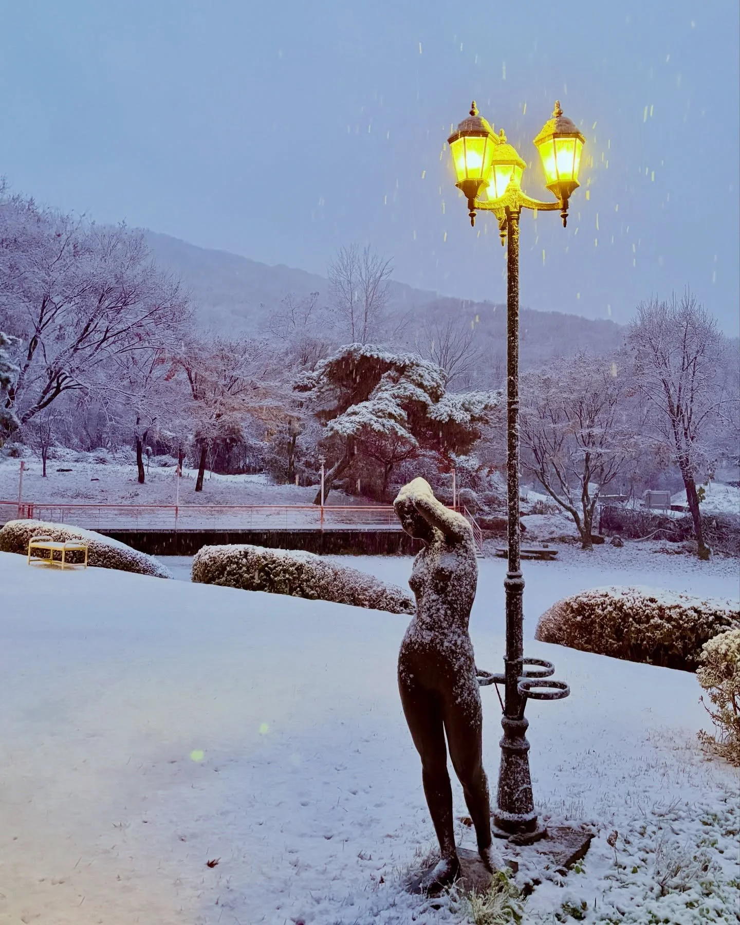 Winter grounds of museum venue for Burnsoo Song exhibition — snow-covered park with classical sculpture and lamppost