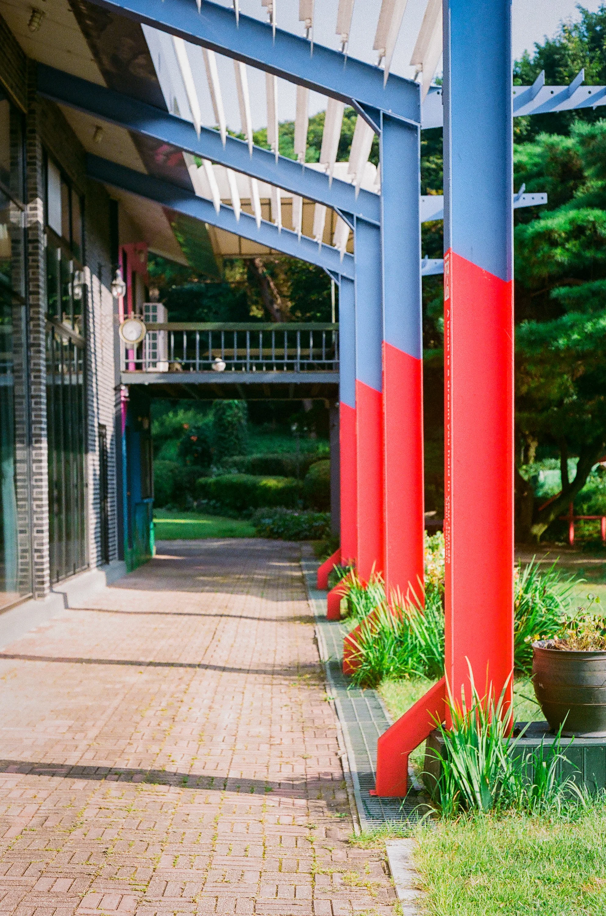 Exterior of gallery venue for Burnsoo Song exhibition — red and blue steel structure, potted plants