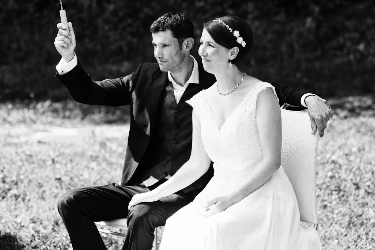 Les mariés assis côte à côte pendant leur cérémonie de mariage en plein air, échangeant un regard complice dans un moment rempli d'émotion en Suisse