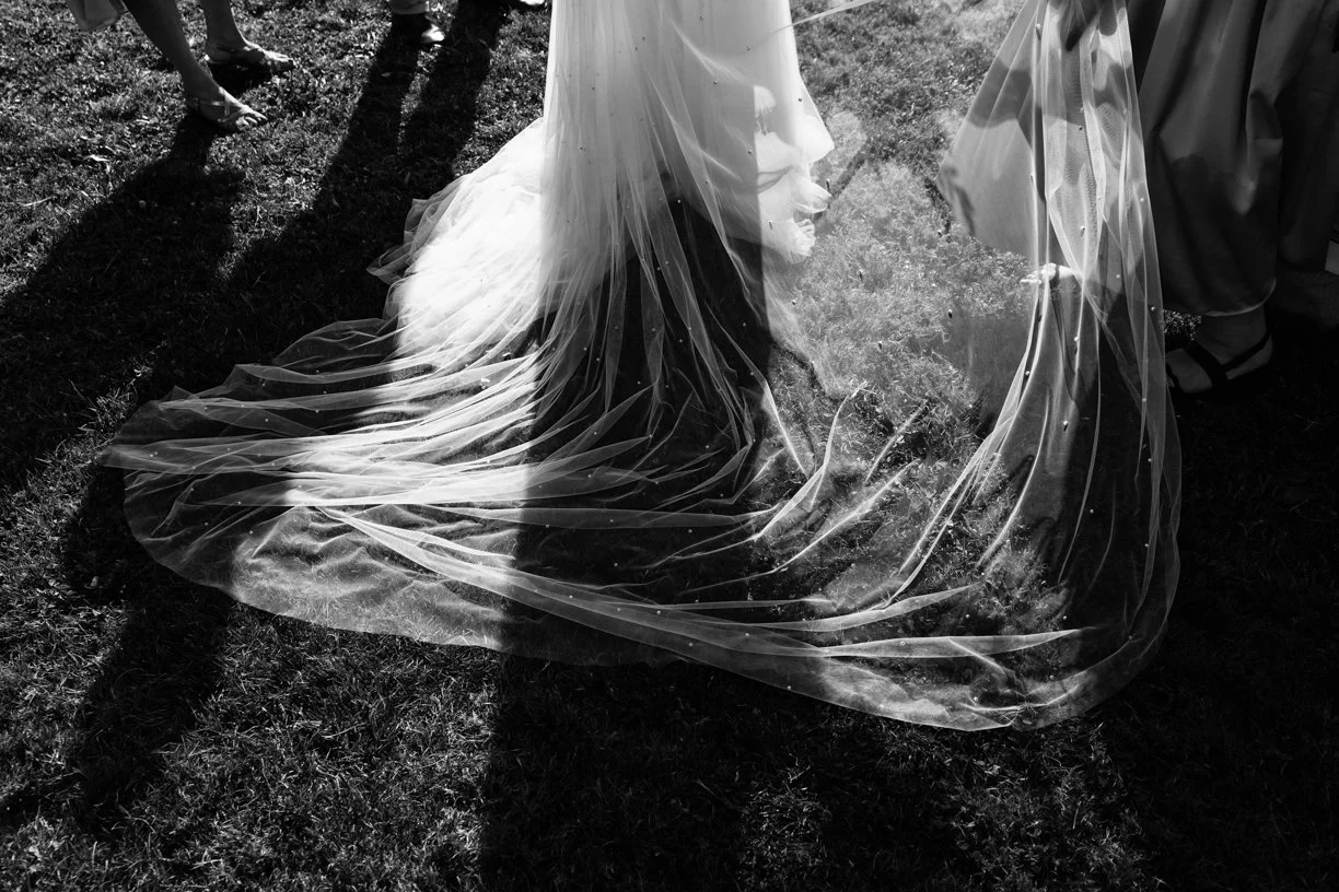 Détail artistique du voile de la mariée illuminé par la lumière naturelle, une photographie de mariage en noir et blanc mettant en valeur les textures, les ombres et l'élégance de la robe.