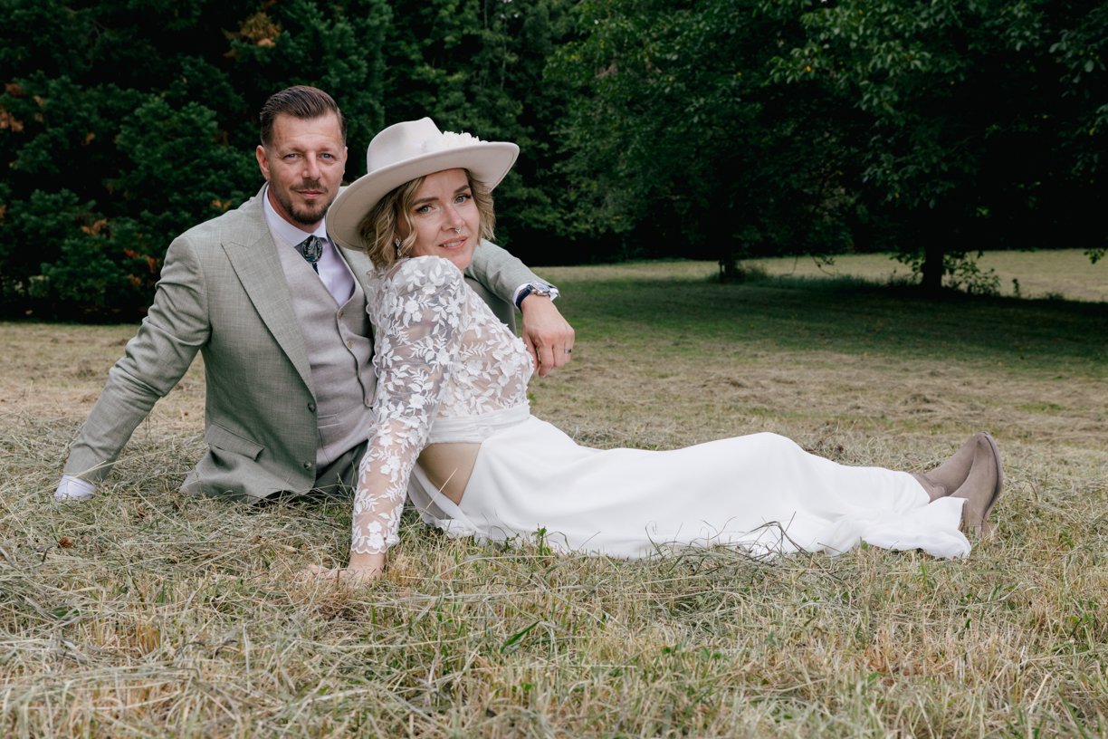 Portrait d'un couple de mariés au style bohème assis dans une prairie, réalisé en lumière naturelle lors d'un mariage en Suisse, entre élégance, complicité et authenticité.
