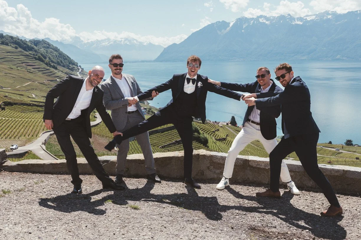 Les garçons d'honneur soulèvent le marié dans les vignobles de Lavaux face au lac Léman et aux Alpes, photographie de mariage spontanée, drôle et élégante réalisée en Suisse
