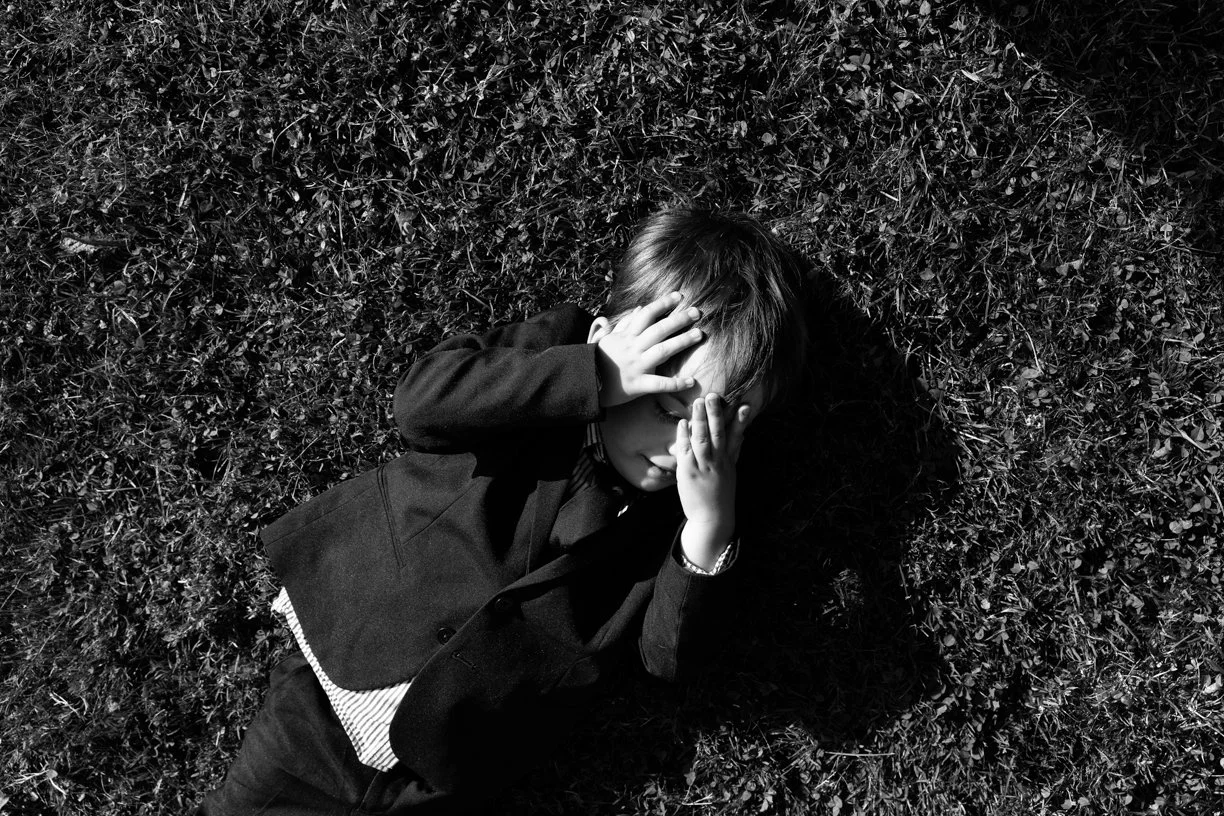 Portrait spontané d'un enfant allongé dans l'herbe pendant un mariage, capturé en noir et blanc avec une approche documentaire mettant en valeur l'innocence et l'émotion de l'instant.