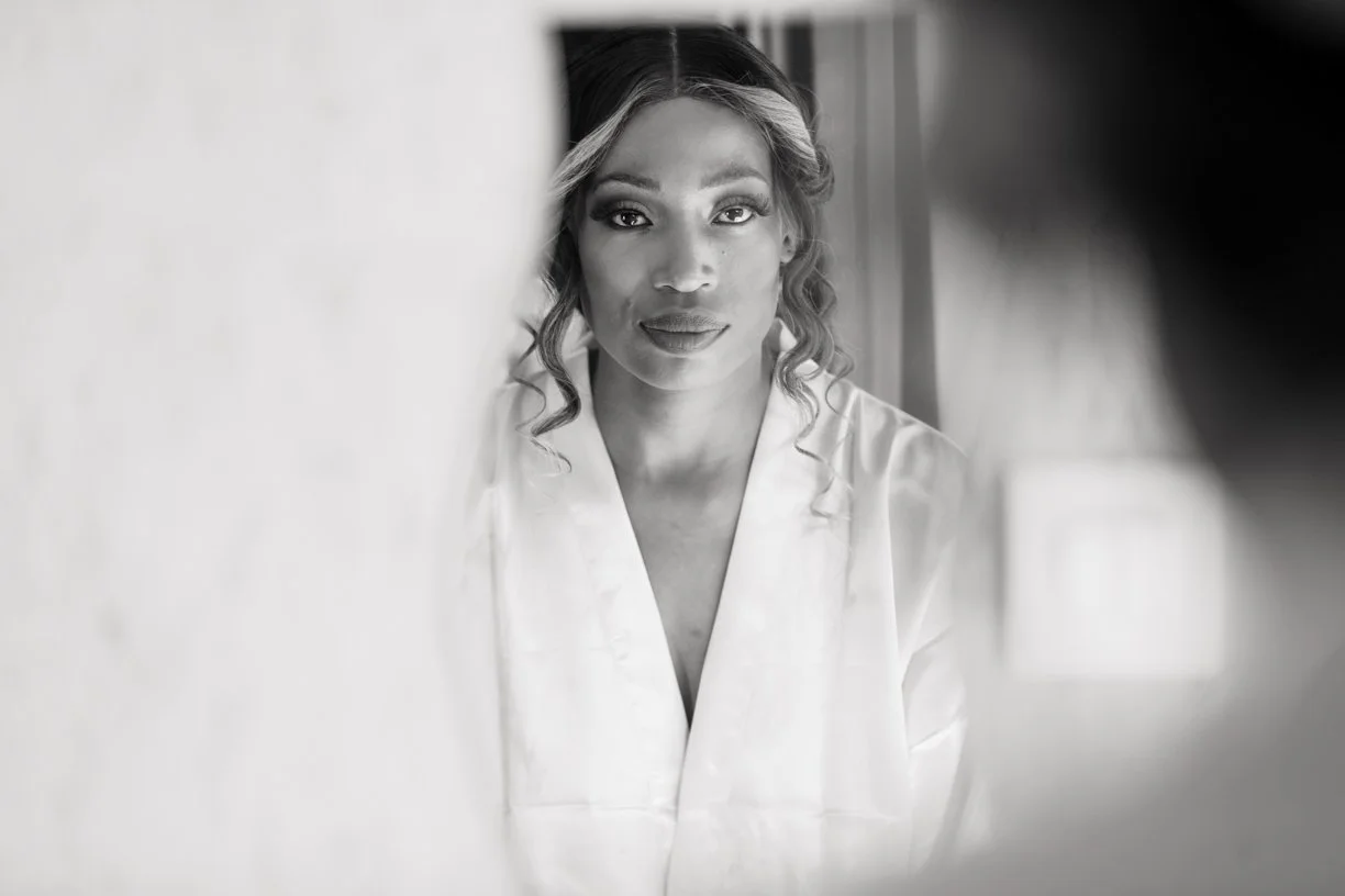 Portrait en noir et blanc d'une mariée pendant les préparatifs de son mariage, capturé à travers un encadrement naturel pour une image élégante et intemporelle.