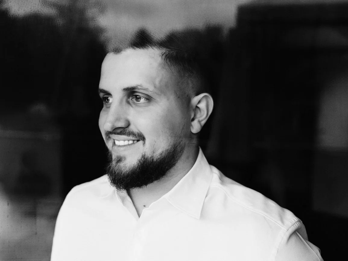 Portrait en noir et blanc du marié pendant les préparatifs de mariage, capturant un sourire naturel et un moment de sérénité avant la cérémonie en Suisse.