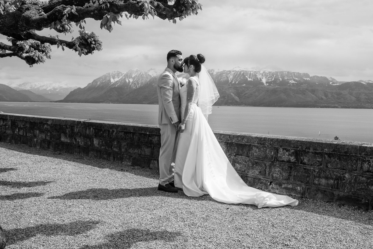 Portrait en noir et blanc d'un couple de mariés face au lac Léman et aux Alpes dans les vignobles de Lavaux, mettant en valeur un paysage emblématique de Suisse.