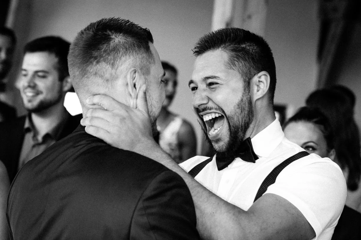 Le marié retrouve un proche dans une étreinte remplie de joie et d'émotion, photographie de mariage en noir et blanc capturant un moment authentique et spontané lors de la réception
