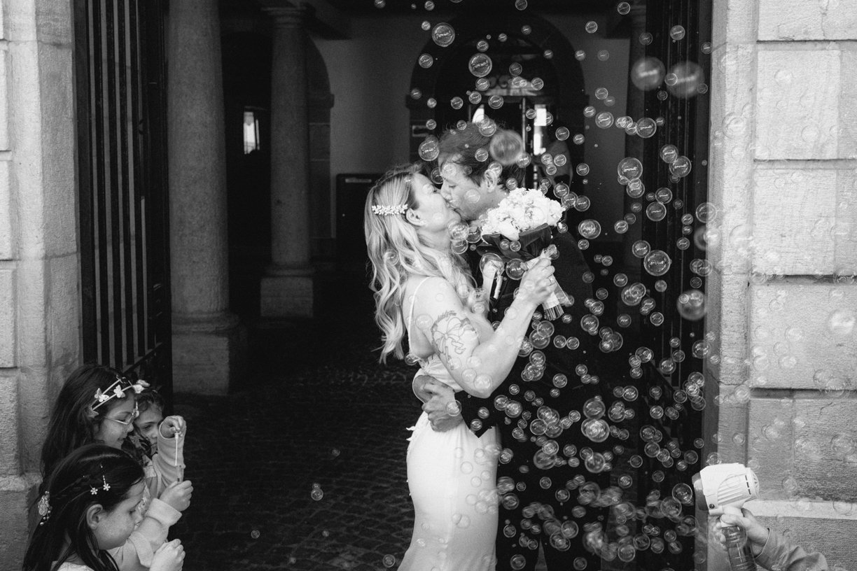 Les mariés s'embrassent à la sortie de la cérémonie sous une pluie de bulles de savon, dans une photo de mariage en noir et blanc capturant un instant de joie et d'émotion
