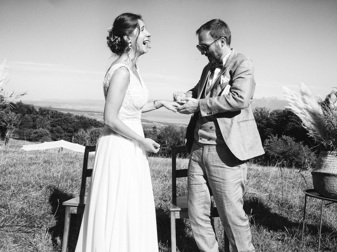 Échange des alliances pendant une cérémonie de mariage en extérieur, capturant un éclat de rire spontané et l'émotion des mariés lors de ce moment unique en Suisse