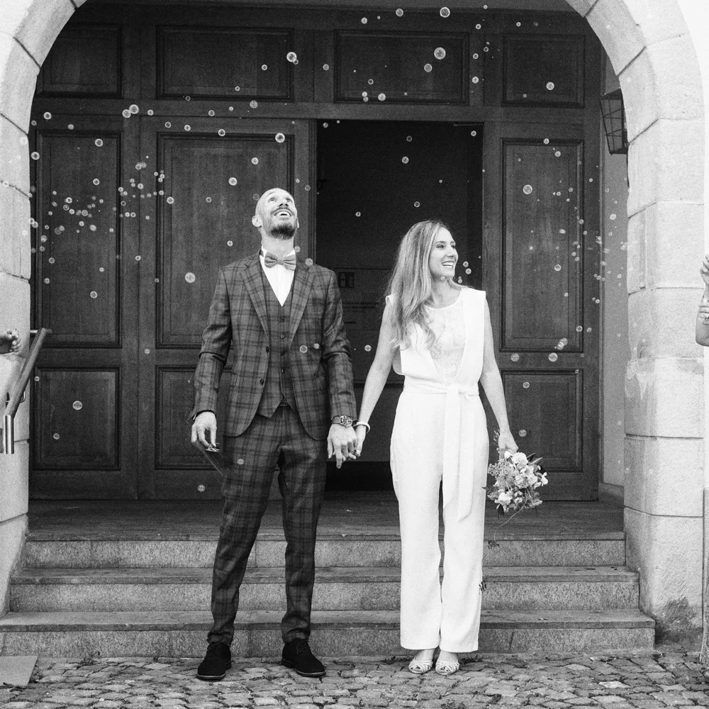 Les mariés sortent de la mairie main dans la main sous une pluie de bulles de savon, capturant un instant de joie et d'émotion lors d'un mariage civil en Suisse