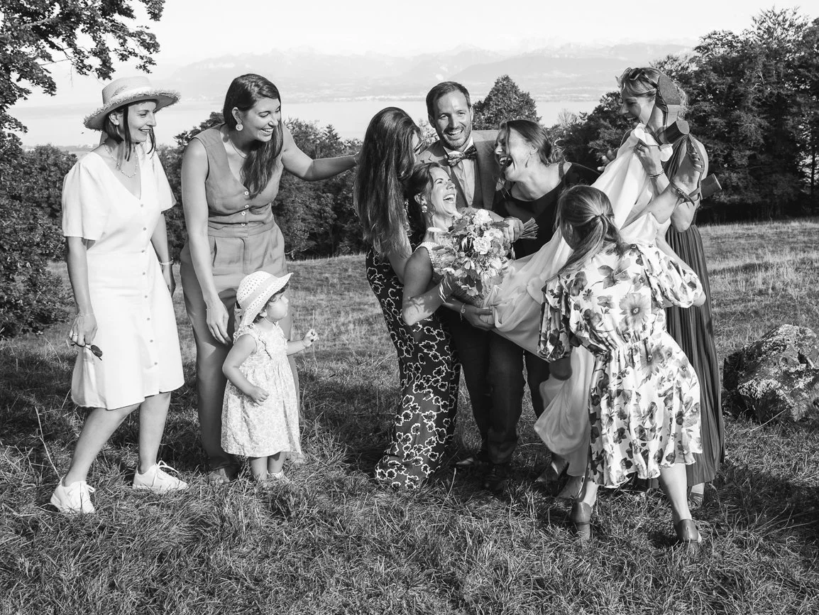 Photo de groupe pleine de rires et de spontanéité réunissant les mariés, leur famille et leurs proches lors d'un mariage en extérieur avec vue sur les montagnes suisses.