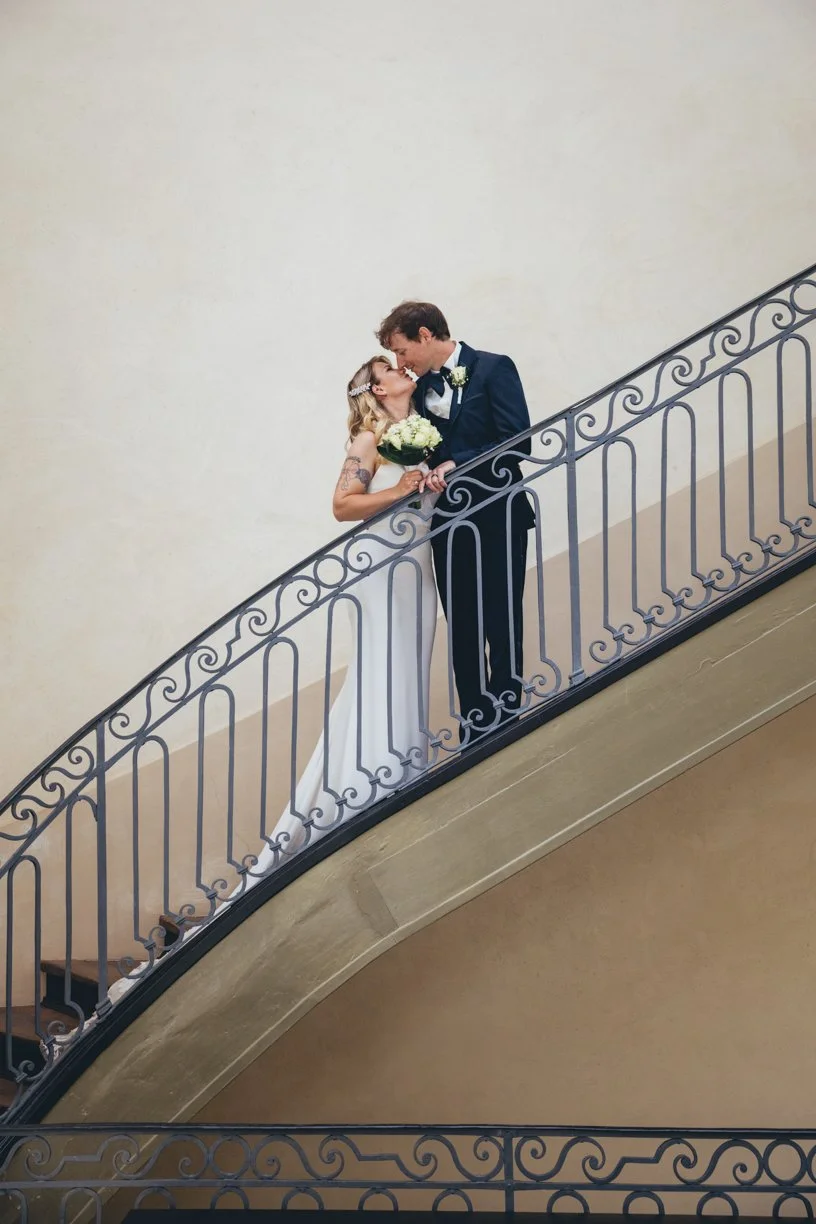 Les mariés s'embrassent sur un élégant escalier aux lignes architecturales, dans un portrait de mariage raffiné réalisé en Suisse mettant en valeur la composition et la symétrie du lieu.