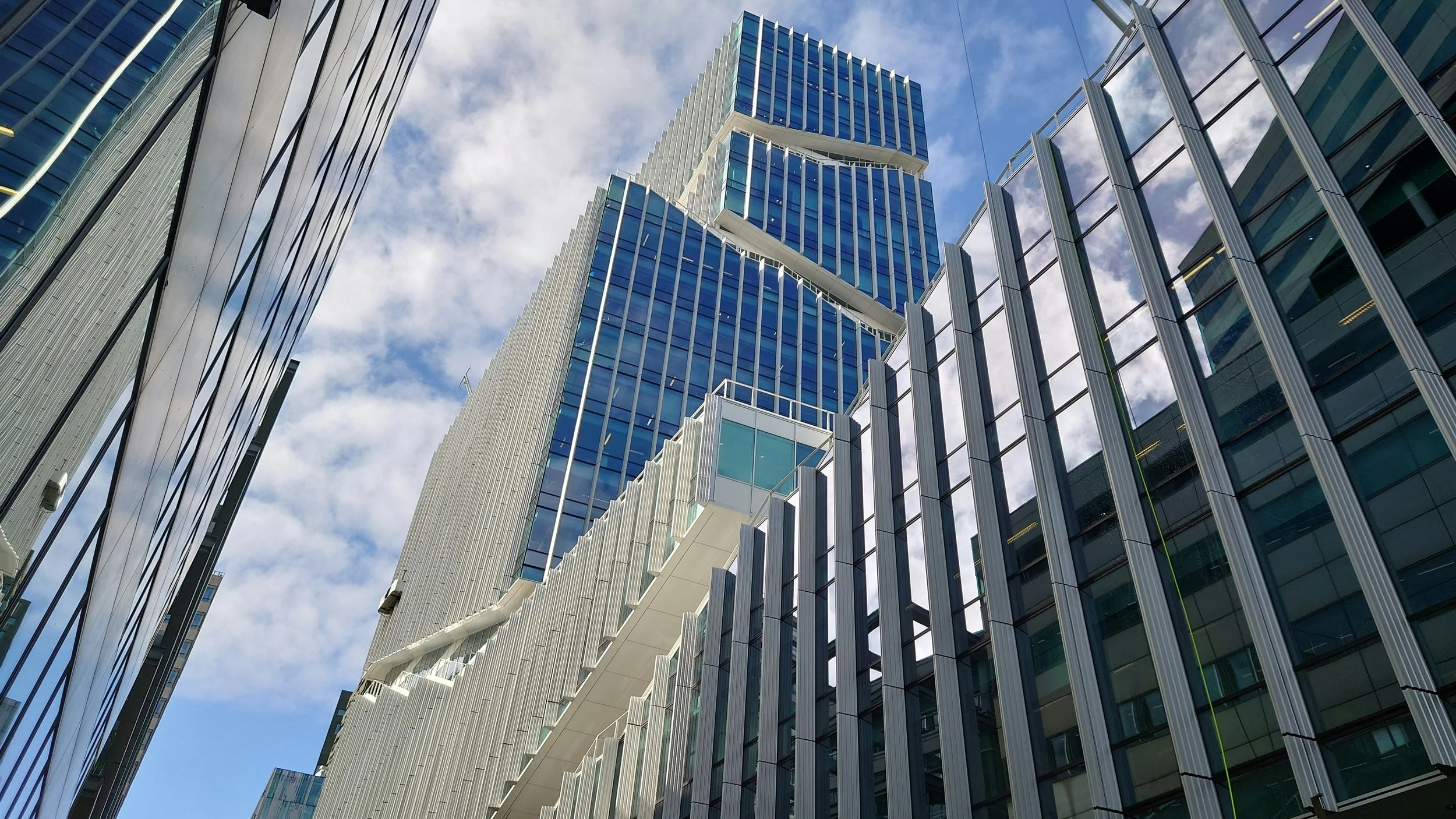 Lage foto van moderne gebouwen met veel glas en metalen oppervlakken, gezien vanaf de grond naar de hemel met wolken.