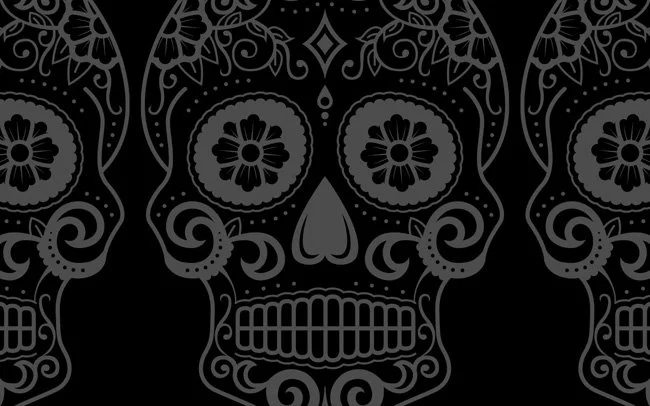 A black and gray decorative skull design with floral and swirl patterns, reminiscent of sugar skulls for Dia de los Muertos.